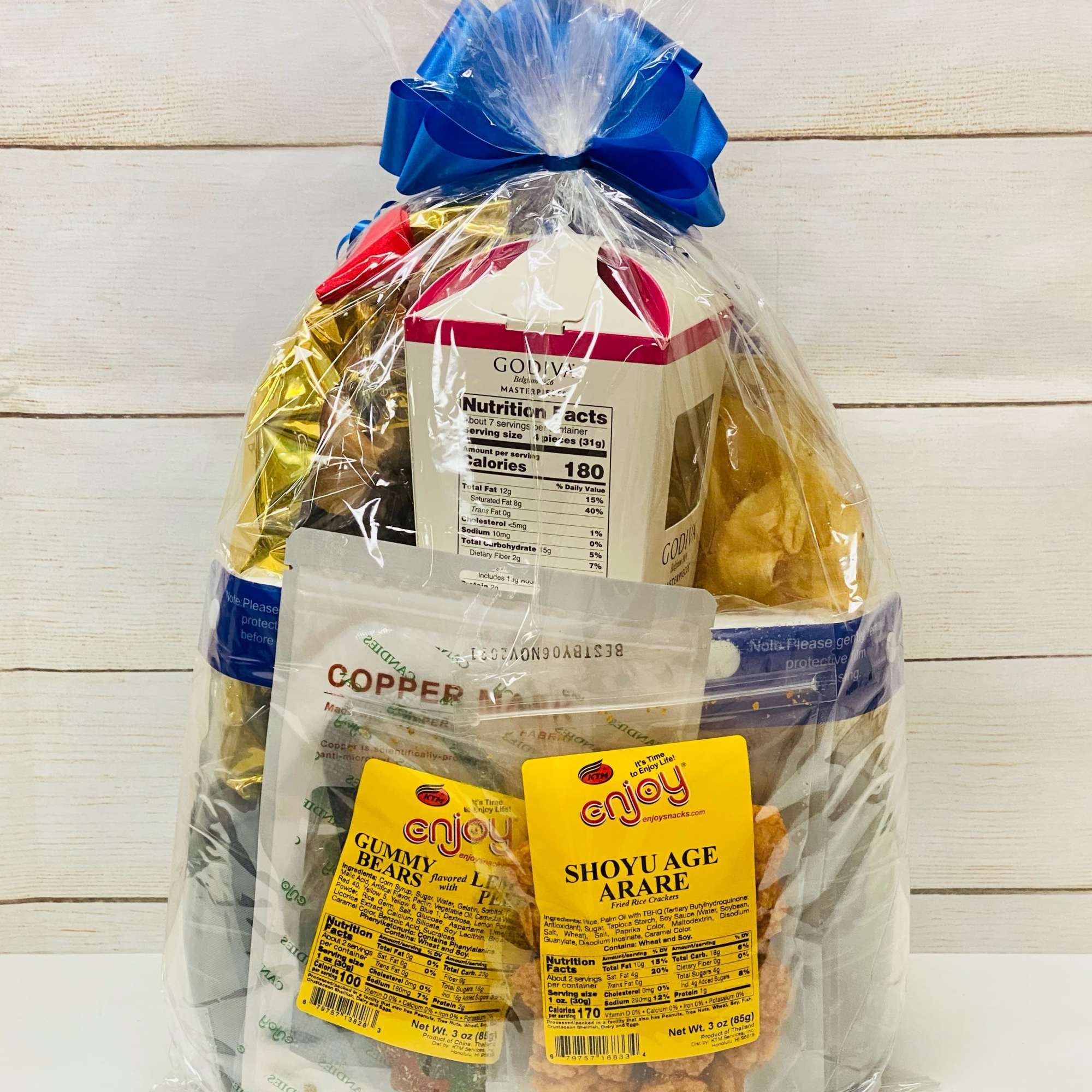 Cellophane-wrapped gift basket of assorted snacks and sweets tied with a blue bow