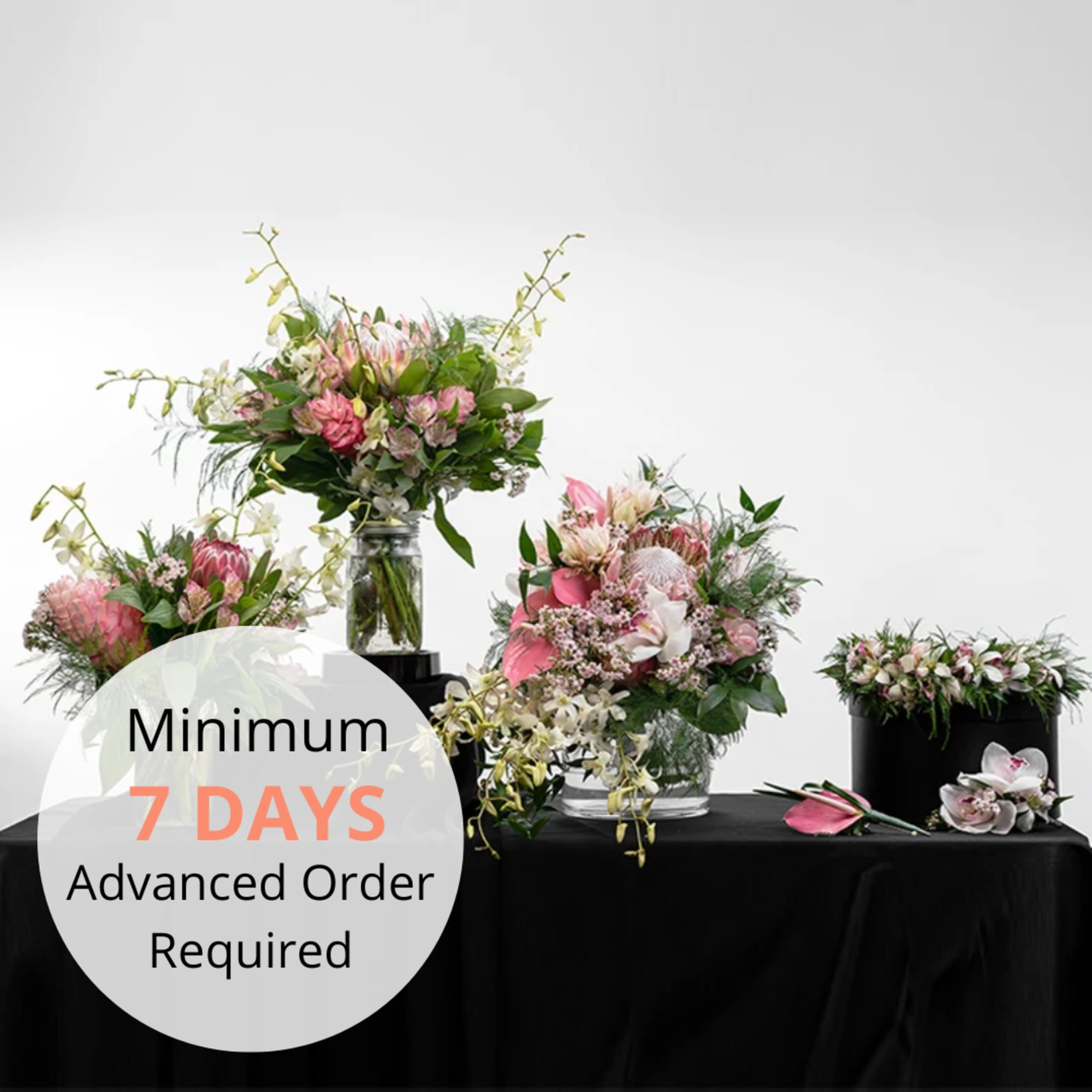 Set of pink and white protea and orchid arrangements in glass and black containers on a black table.