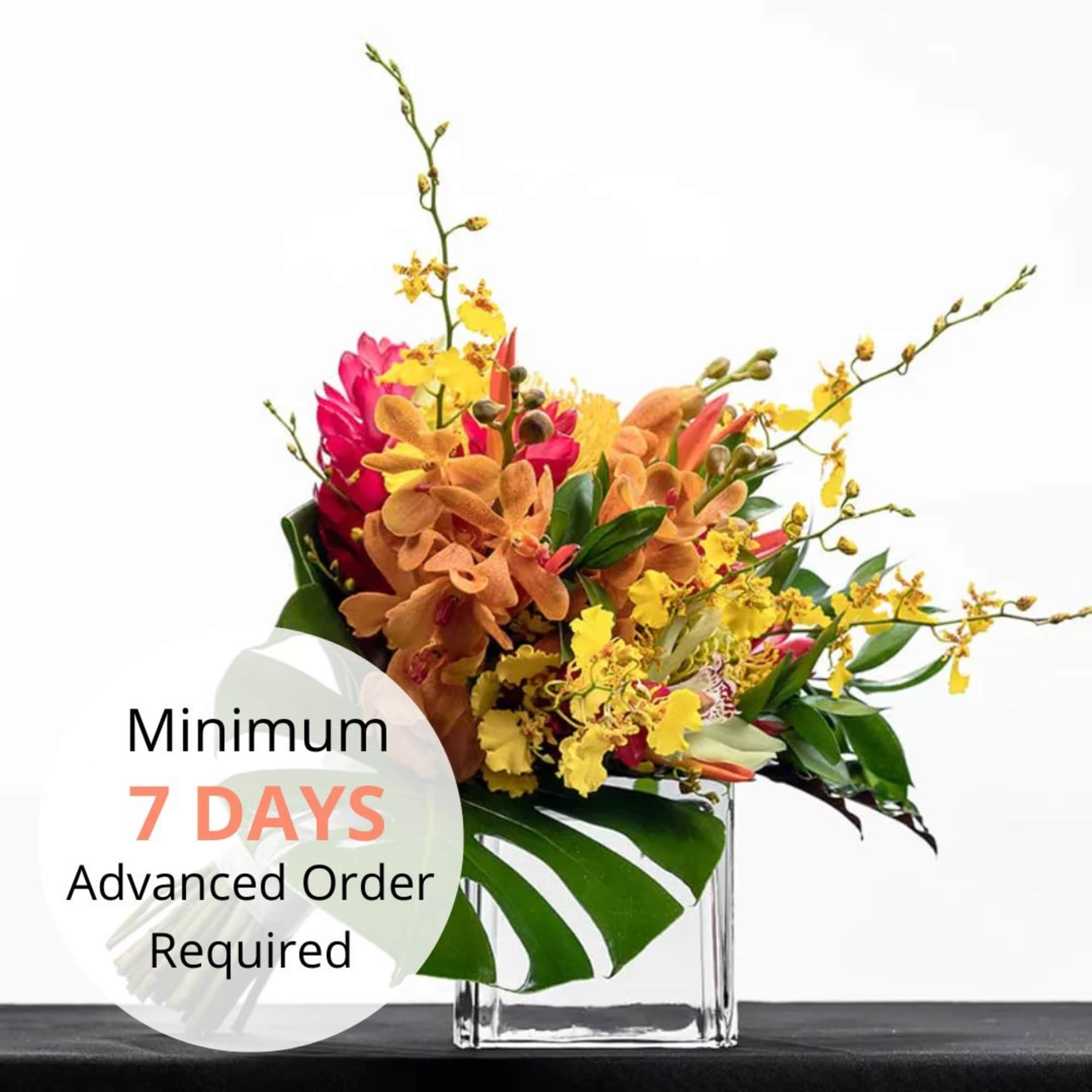 Tropical arrangement of yellow and orange orchids with pink blooms in a clear glass cube vase
