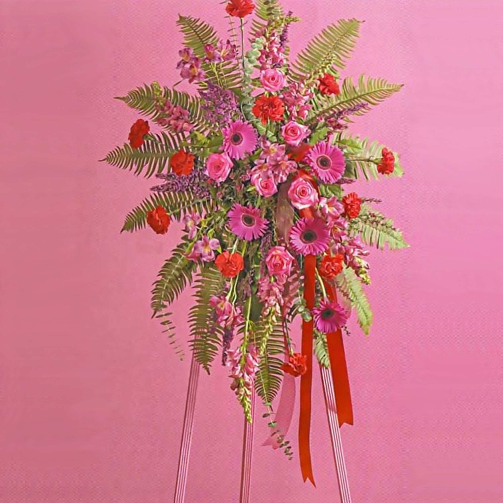 Tall pink and red standing spray with gerbera daisies and roses on an easel with red ribbon