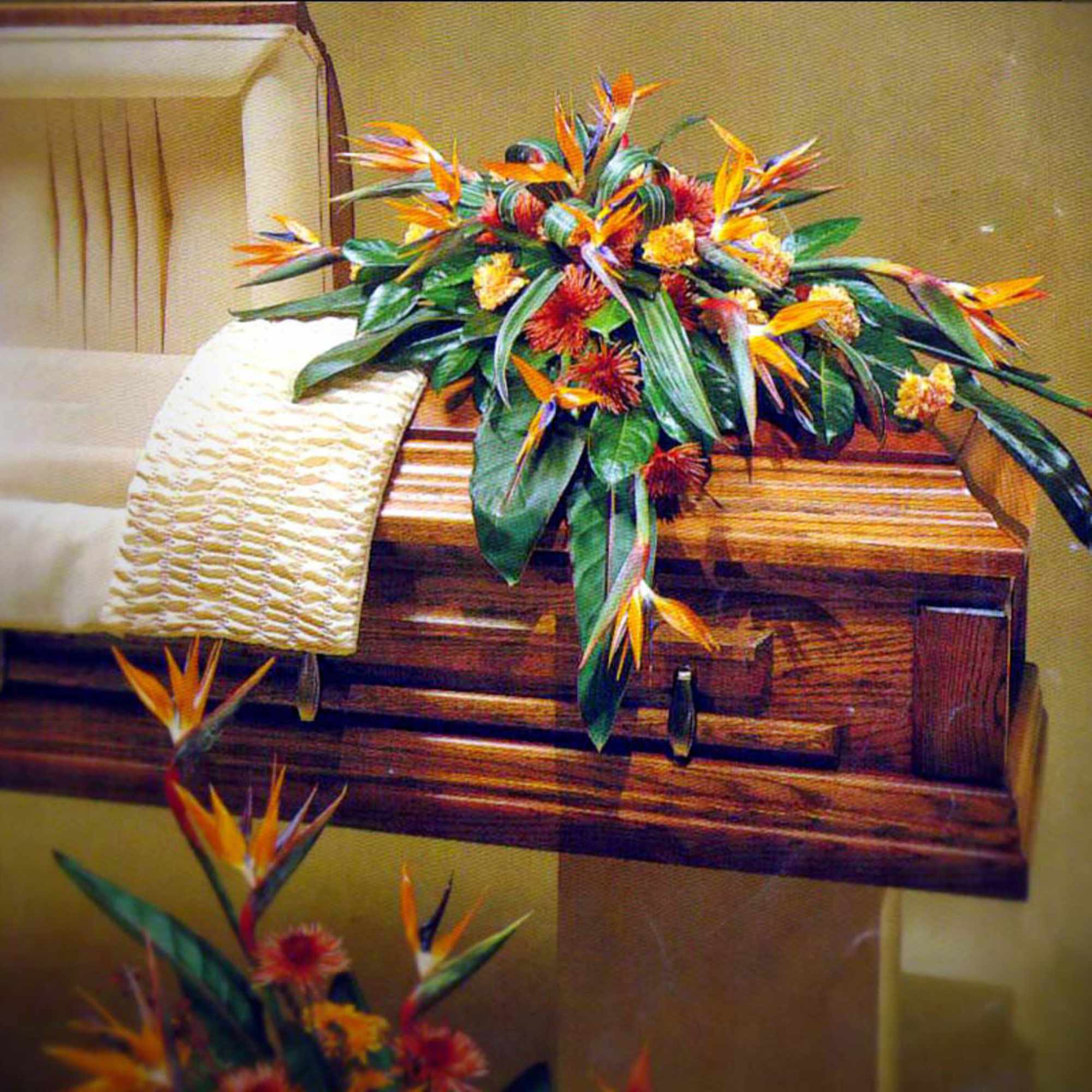 Tropical orange and yellow casket spray with Birds of Paradise on a polished wood casket.