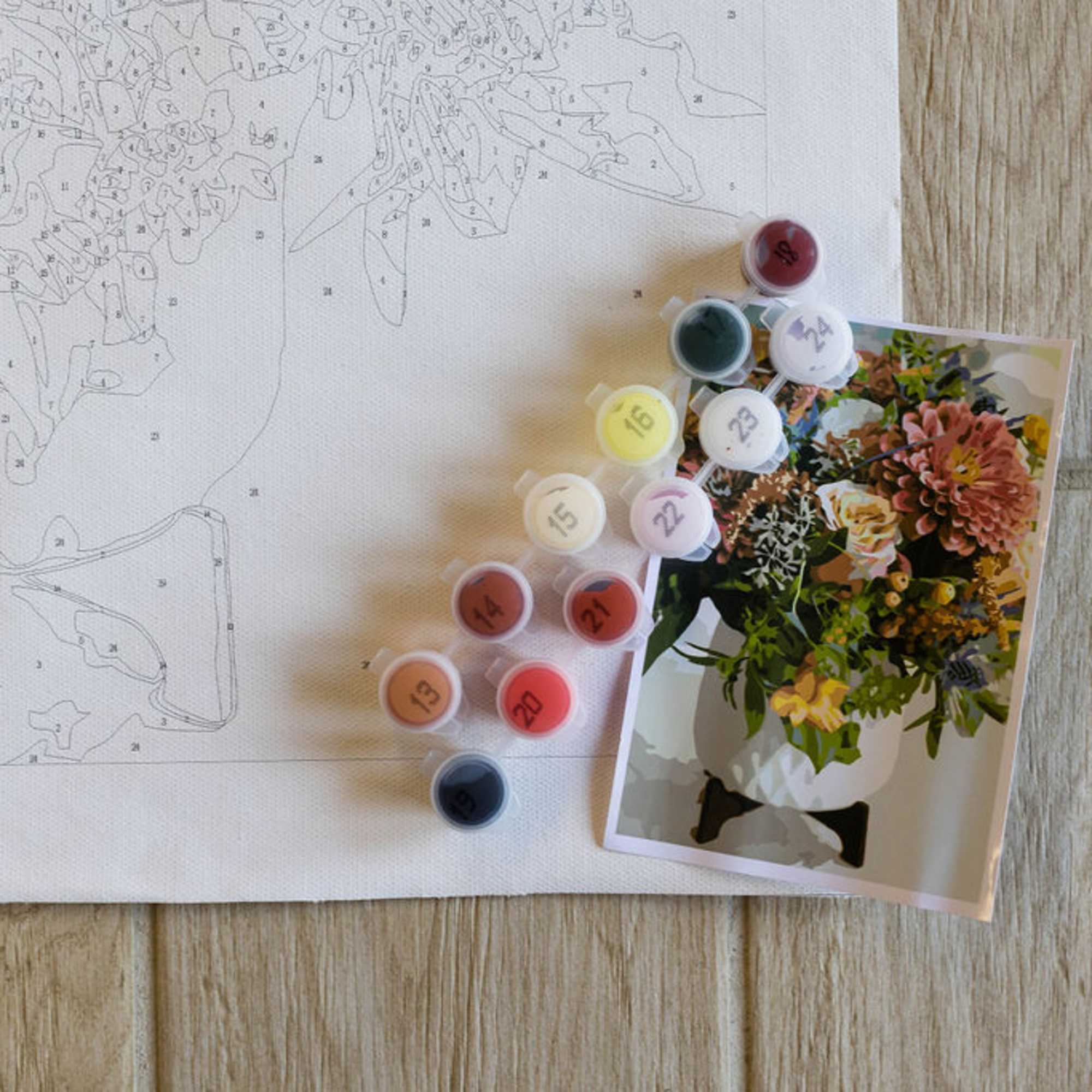 Paint-by-number canvas with numbered sections and paint pots beside a flower reference card