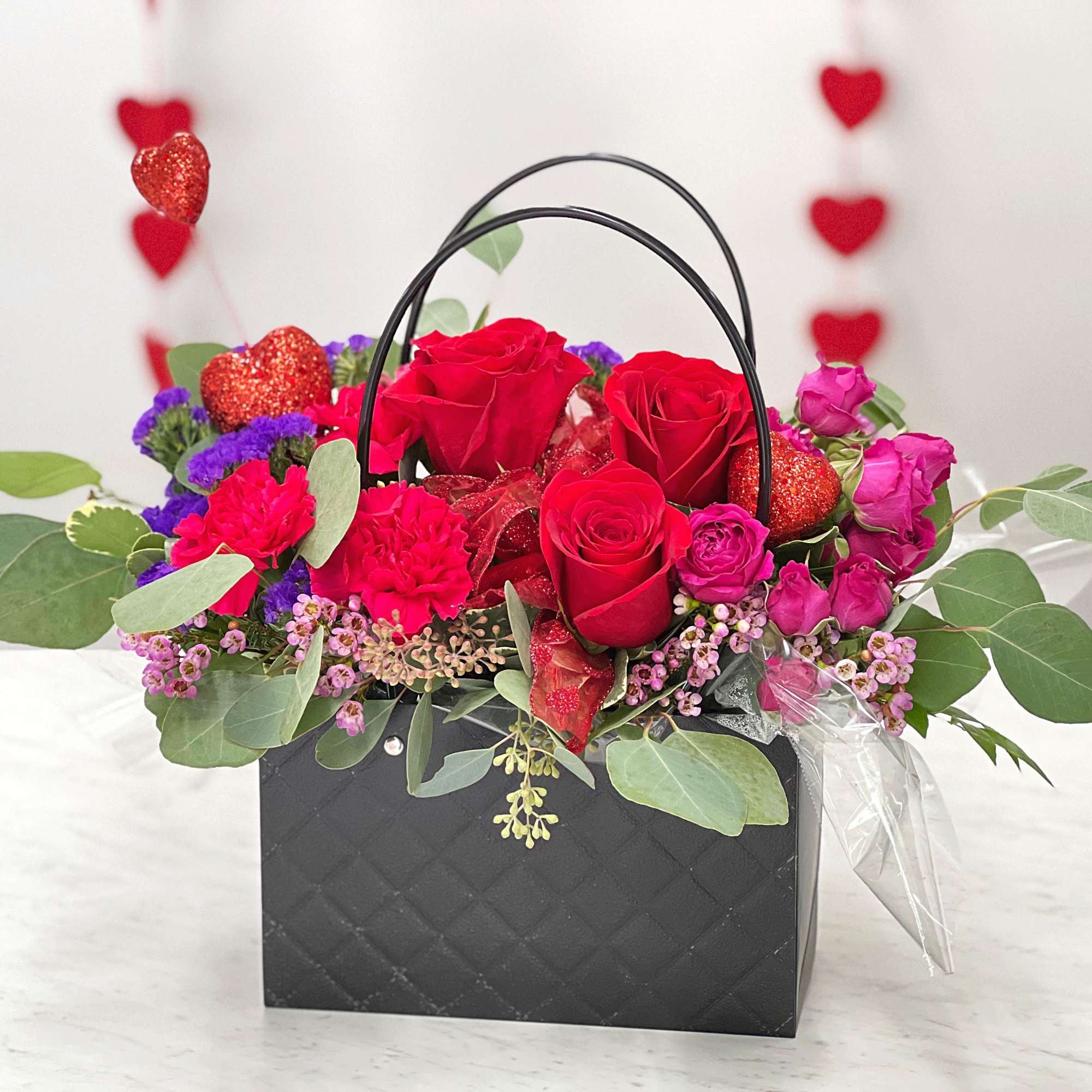 Red roses and pink flowers in a black handled box