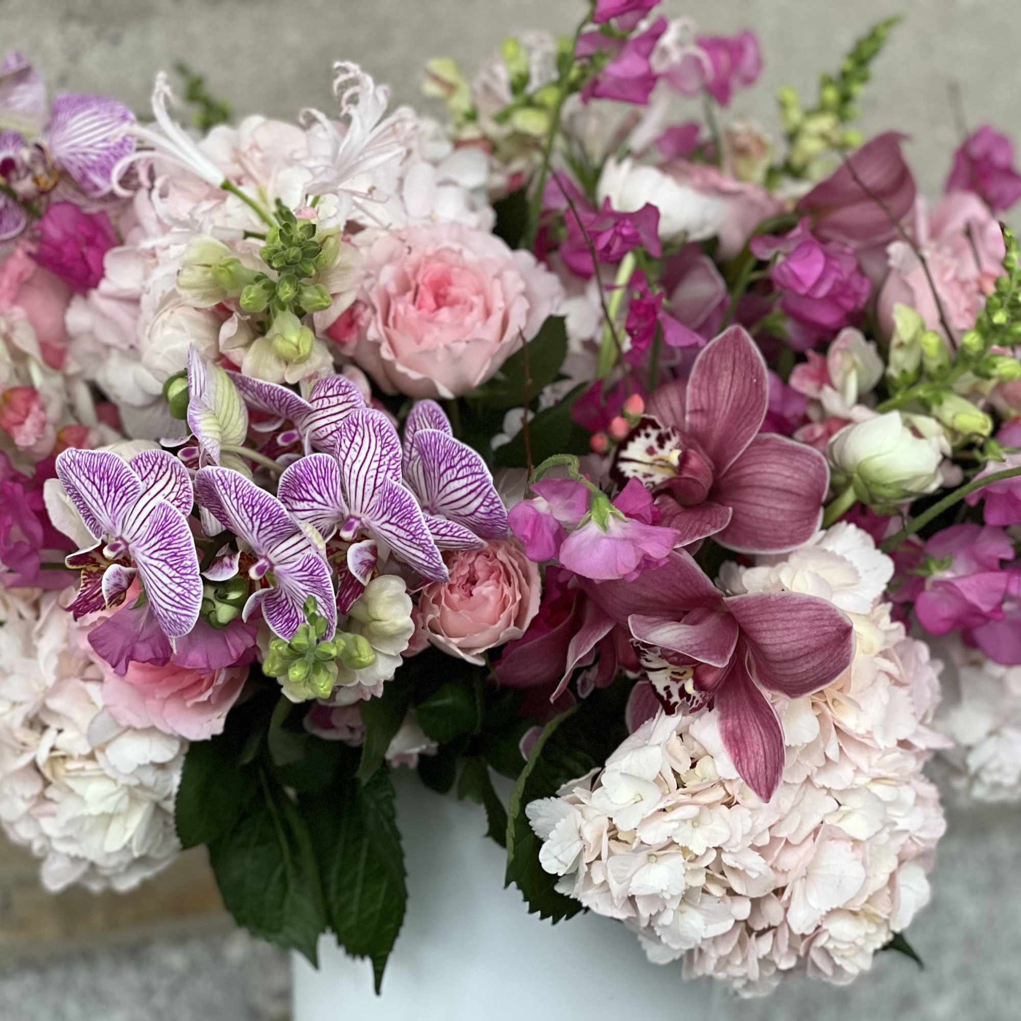 Pink and white floral arrangement with orchids, roses, and hydrangeas in a vase