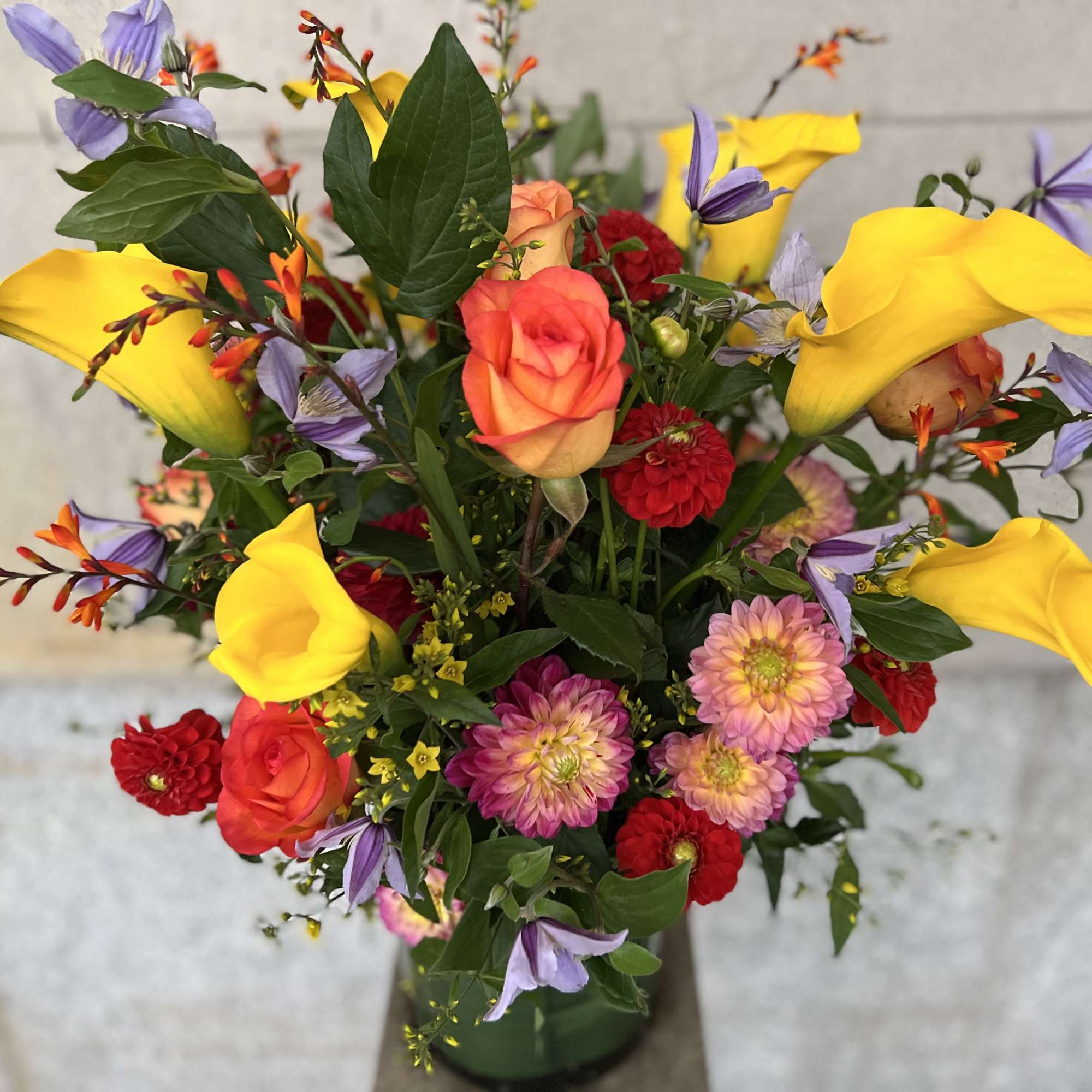 Colorful bouquet with yellow calla lilies, roses, and purple flowers in a vase