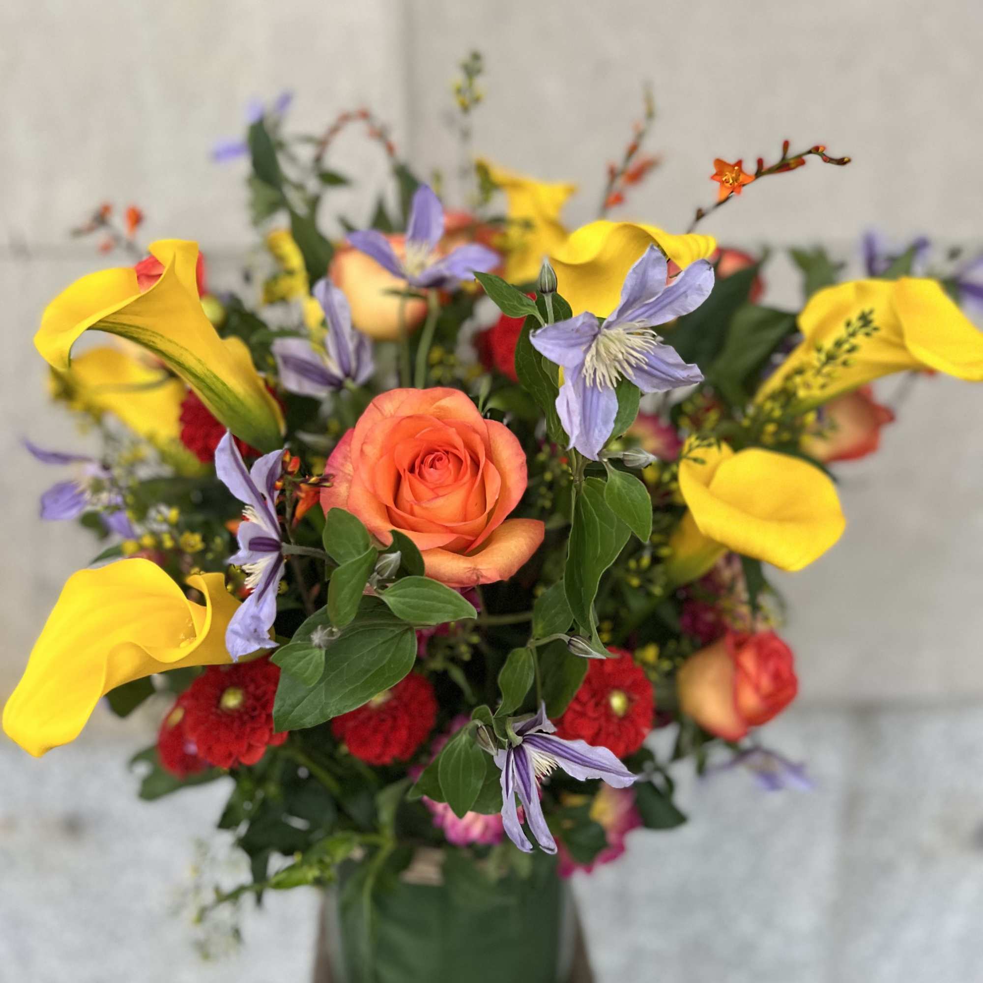 Mixed bouquet with orange roses, yellow calla lilies, and purple flowers in a green vase