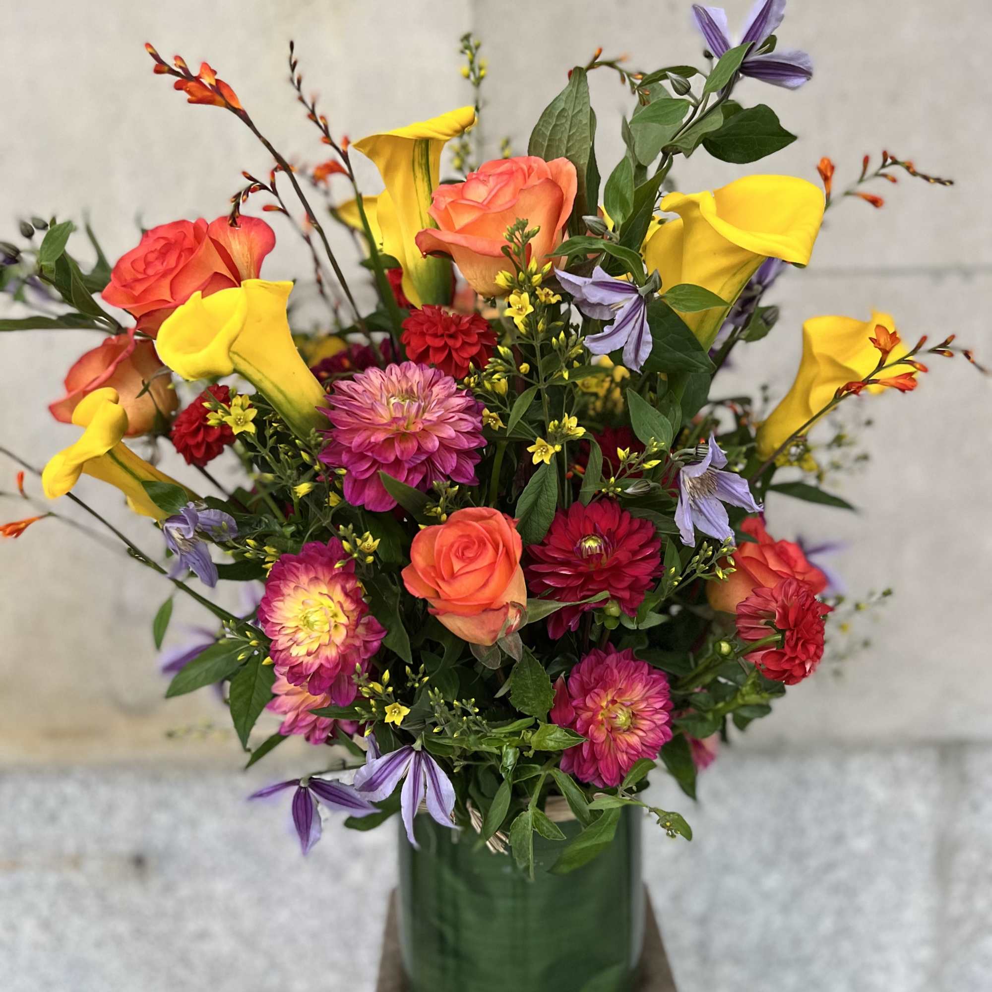 Colorful mixed bouquet in a green glass vase with roses, calla lilies, and daisies