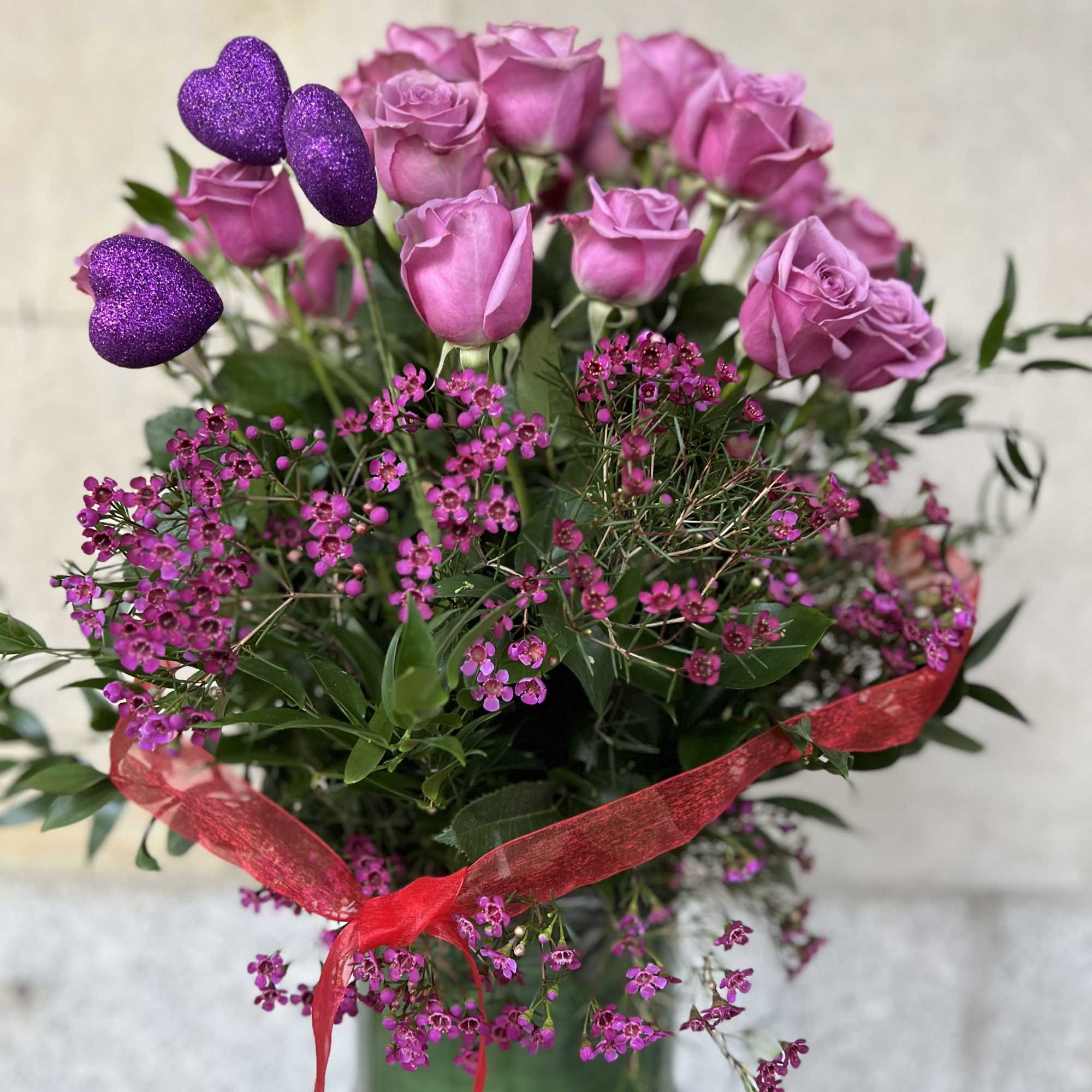 Pink roses in a glass vase with purple glitter hearts and a red ribbon