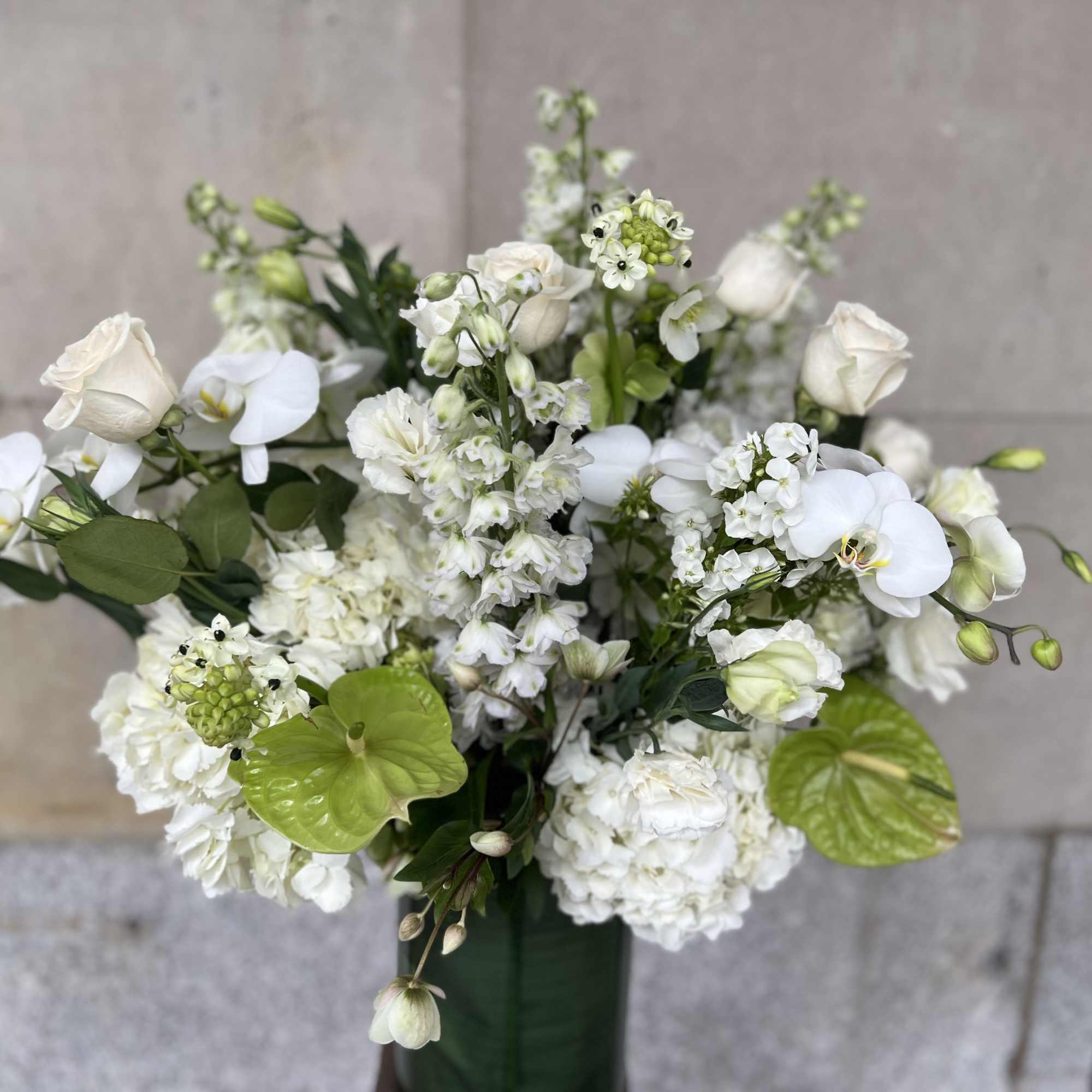 White floral arrangement with orchids and roses in a tall vase