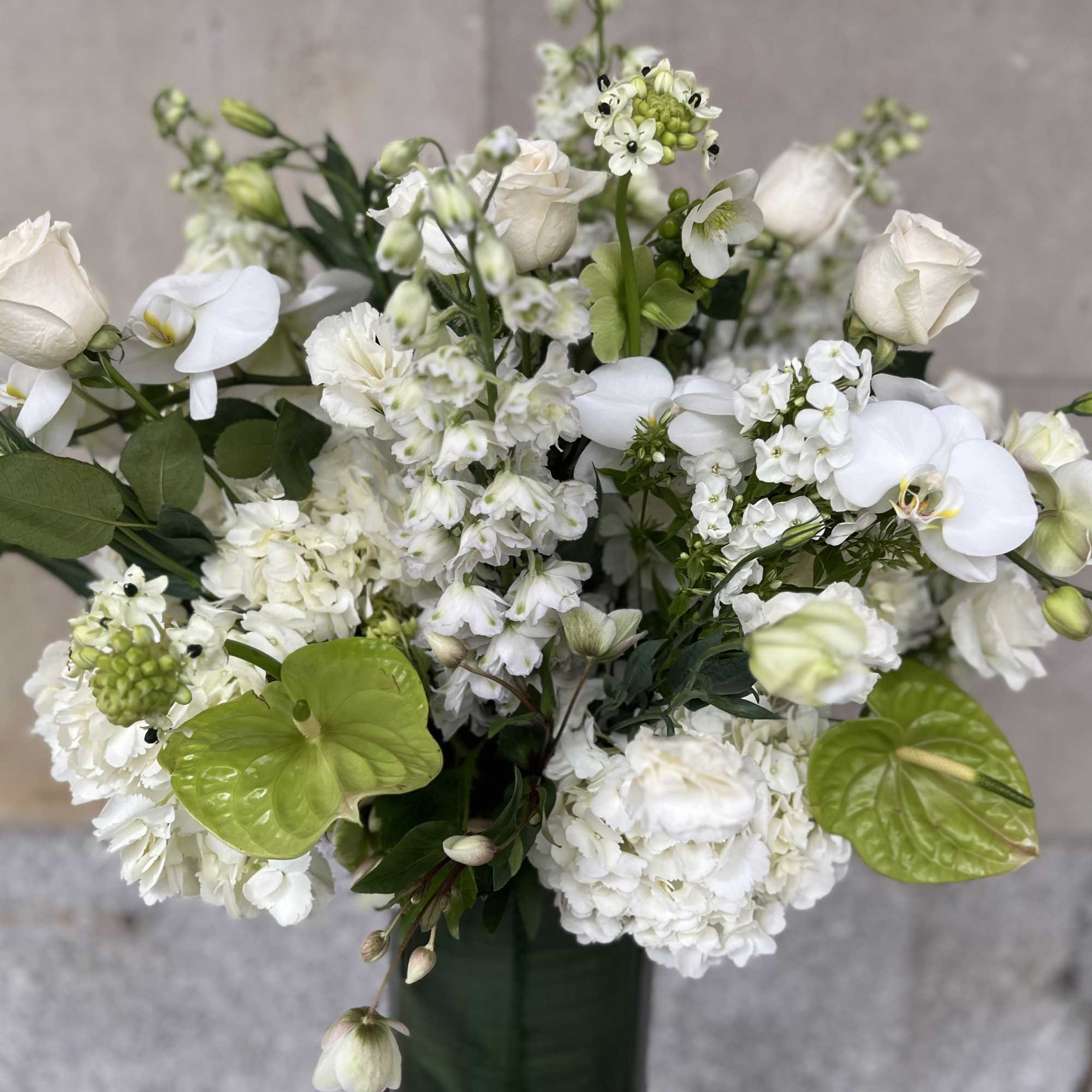 White floral arrangement with roses, orchids, and green accents in a vase