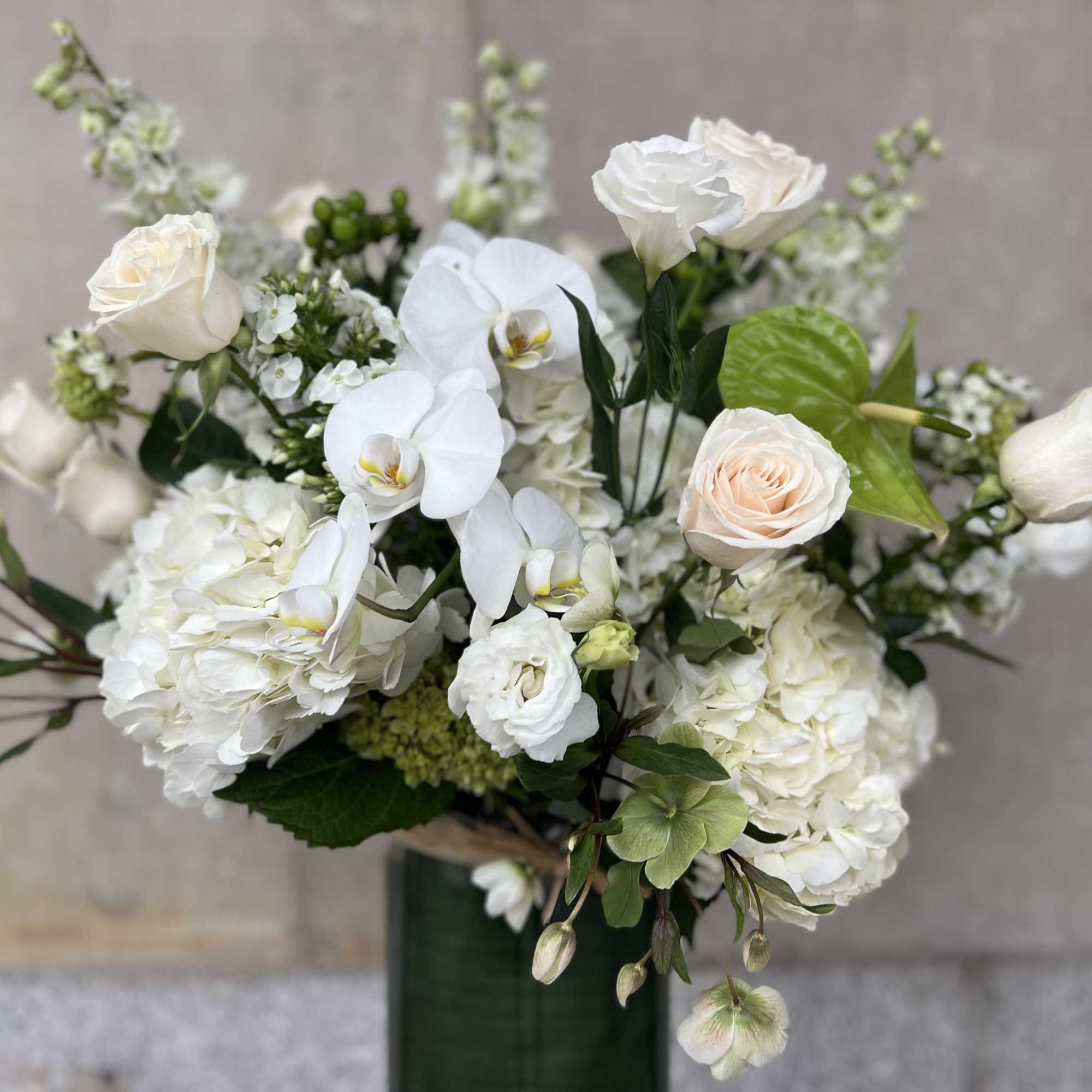 White floral arrangement with roses, orchids, and hydrangeas in a green vase