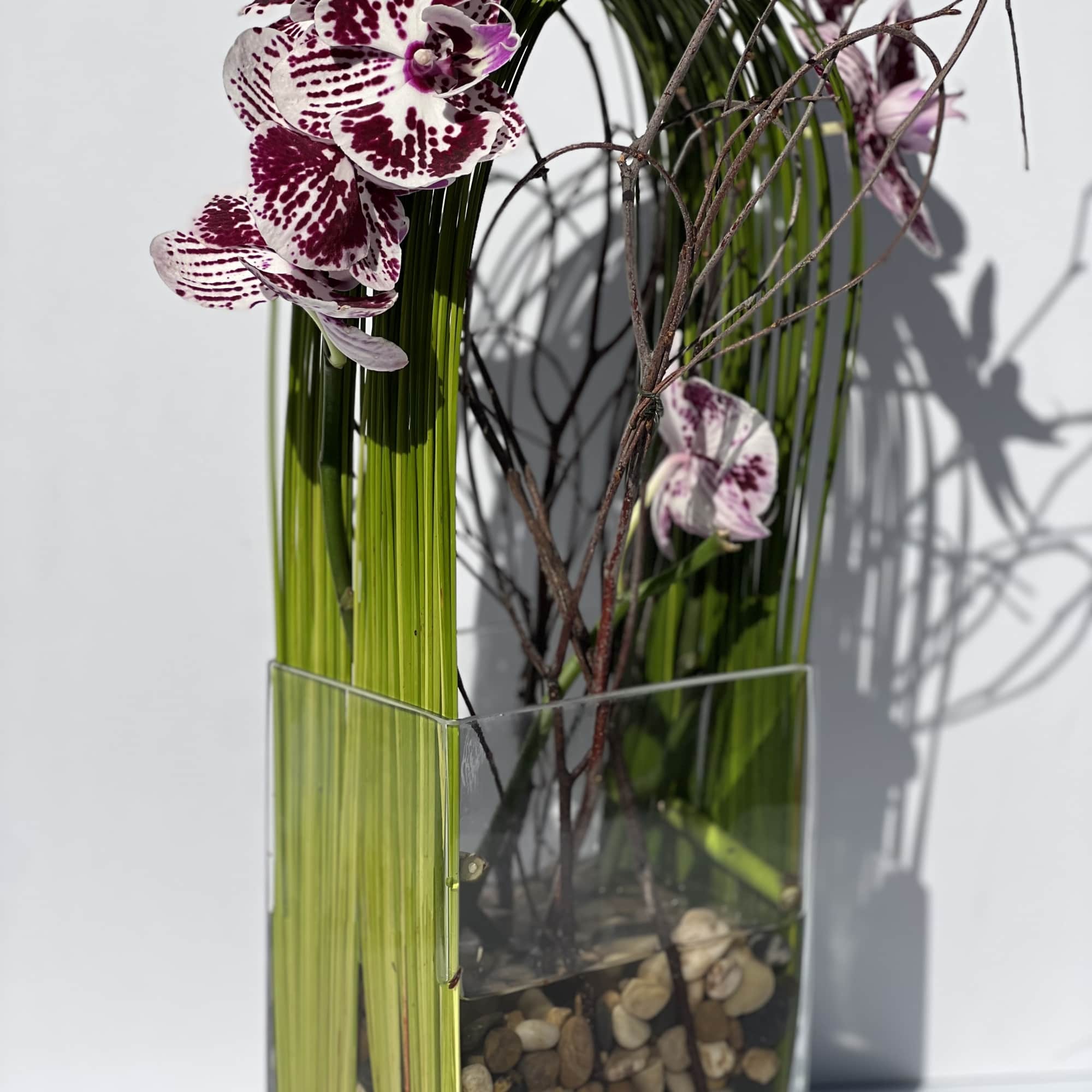 Purple-spotted orchids in a tall glass vase with decorative branches