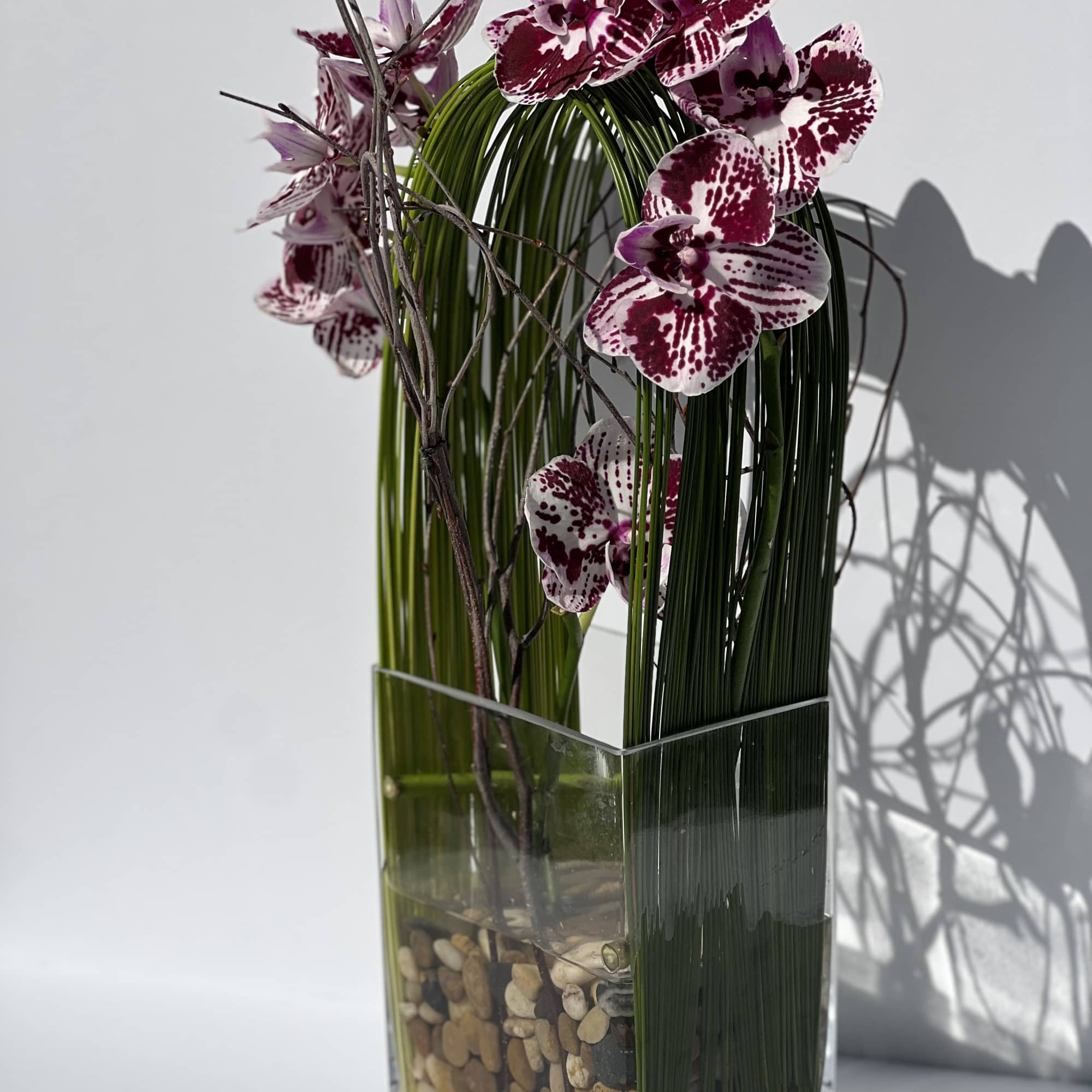 Spotted purple orchids in a tall clear glass vase with pebbles