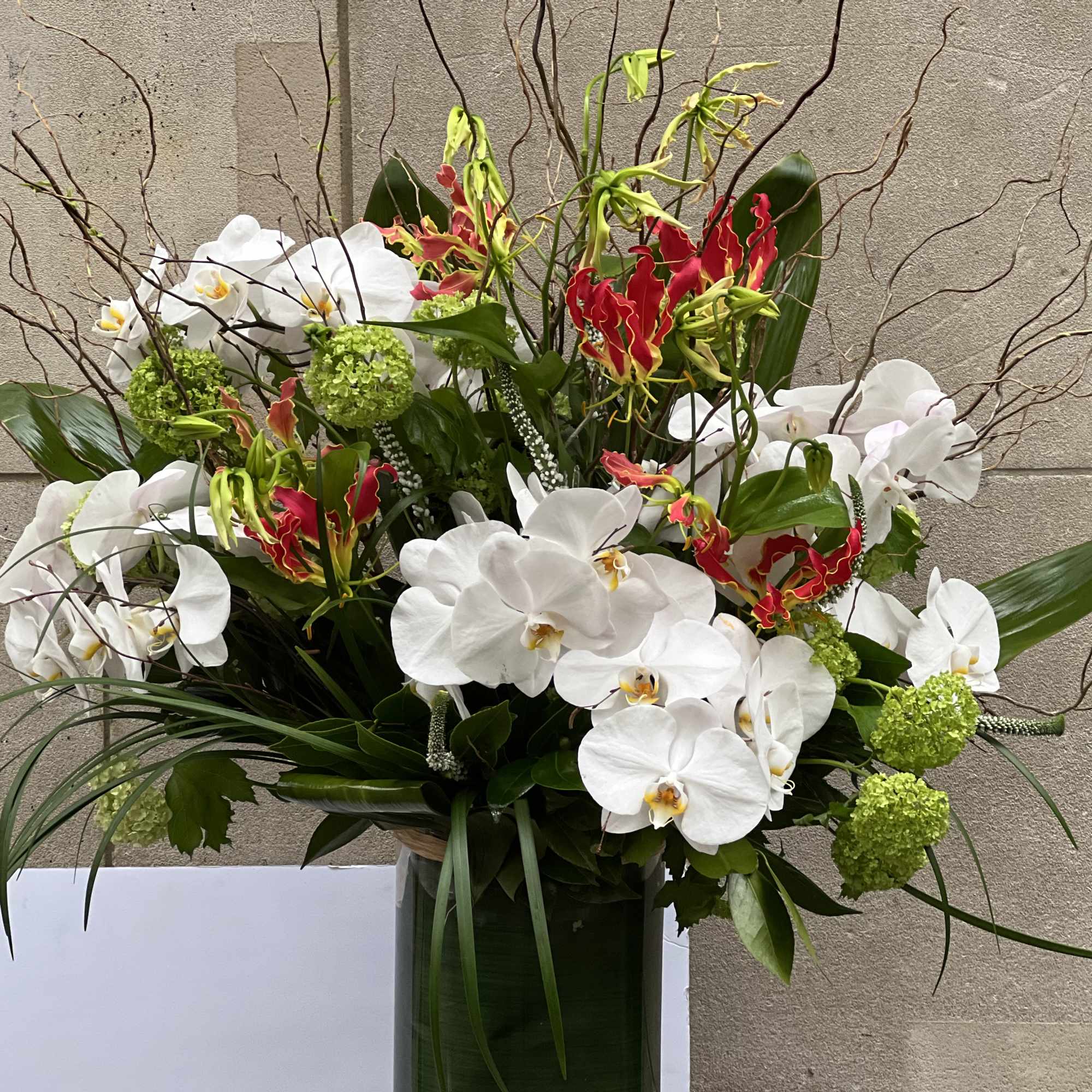 CYLINDRICAL VASE WITH JAPANESE GLORIOSA, WHITE PHALAENOPSIS ORCHIDS, VIBURNUM, THAI LEAF, AND