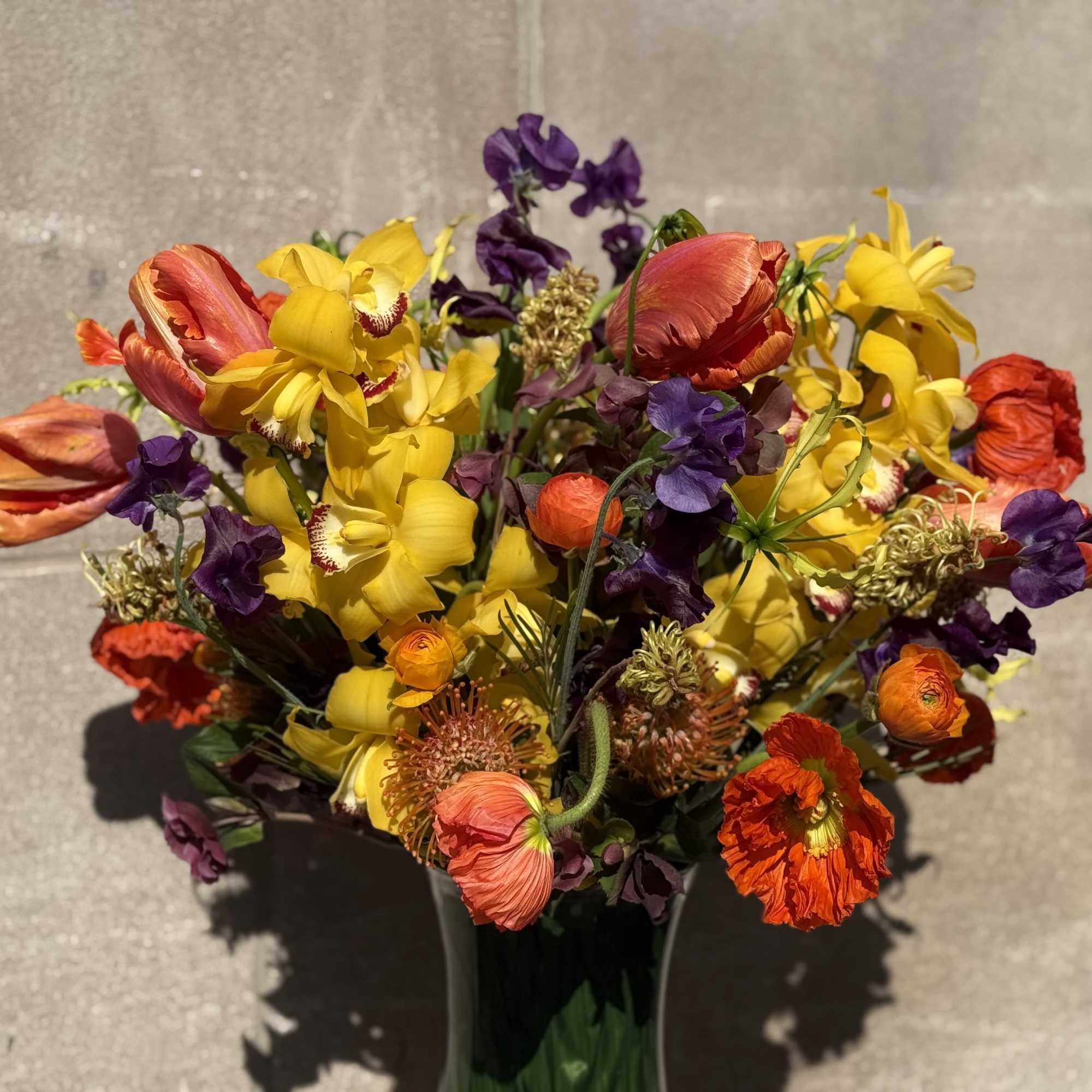 Bouquet of yellow, orange, red, and purple flowers in a dark vase