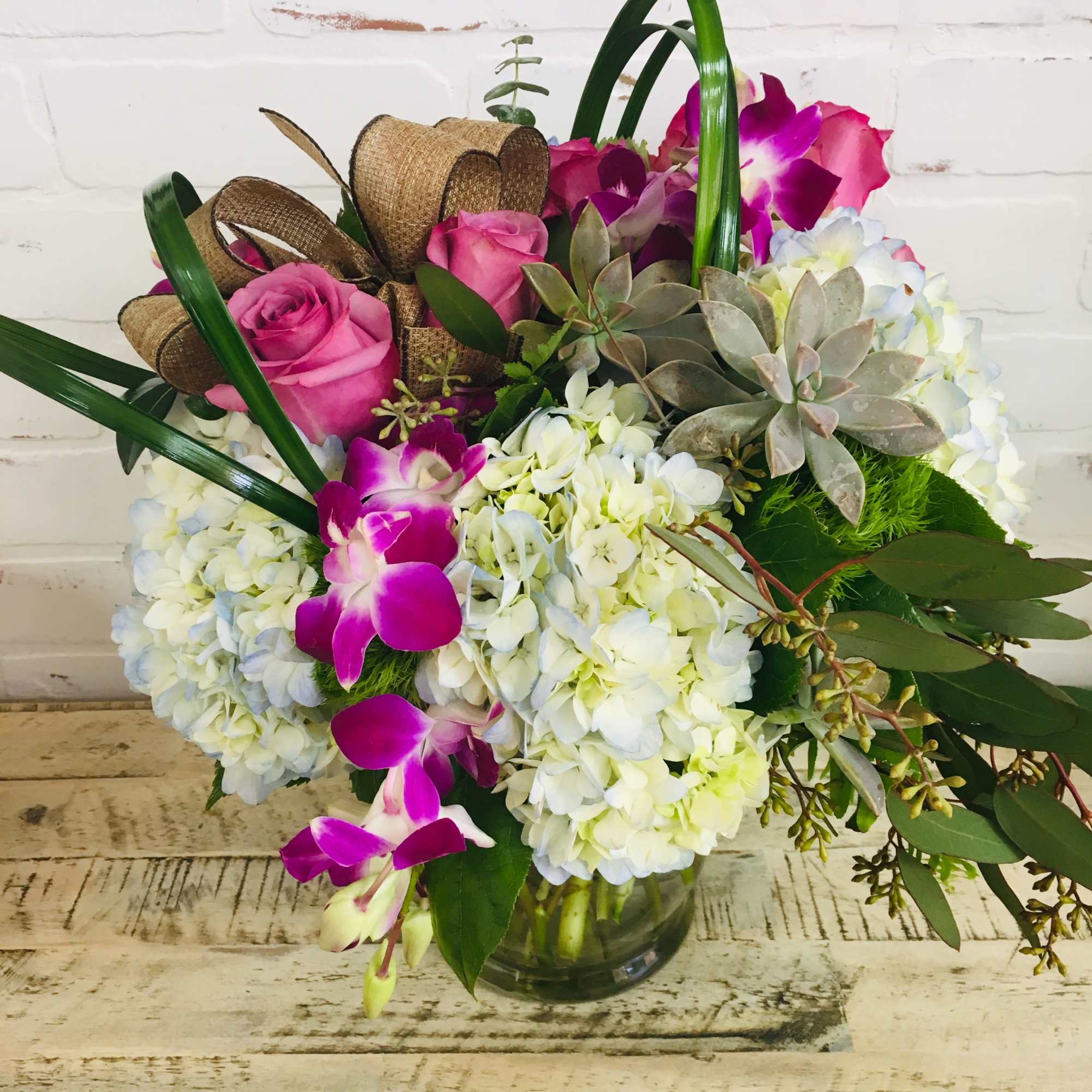 Pink roses and purple orchids arranged with white hydrangeas in a glass vase