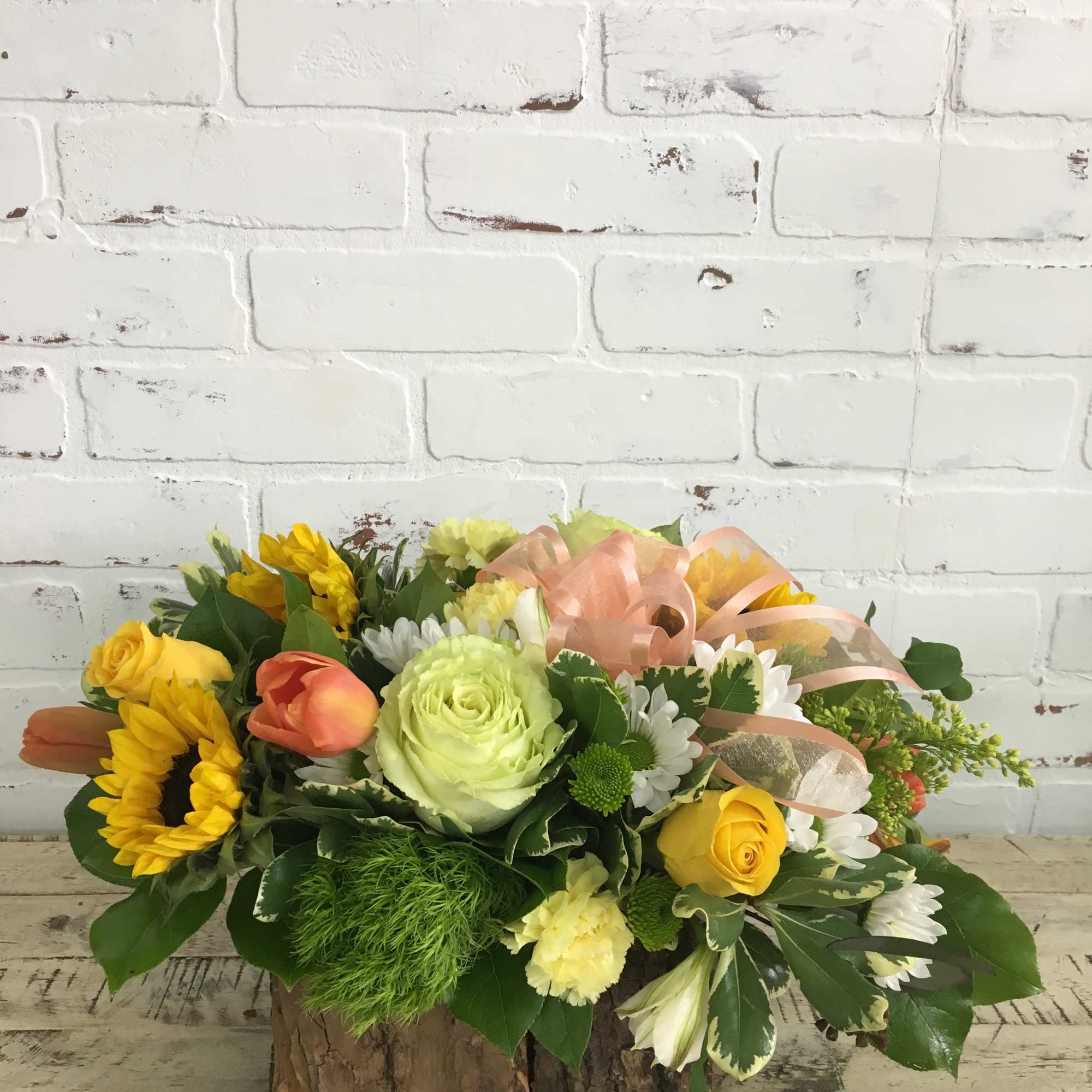 Low rustic centerpiece with yellow sunflowers, roses, tulips, and white daisies in a bark-covered container