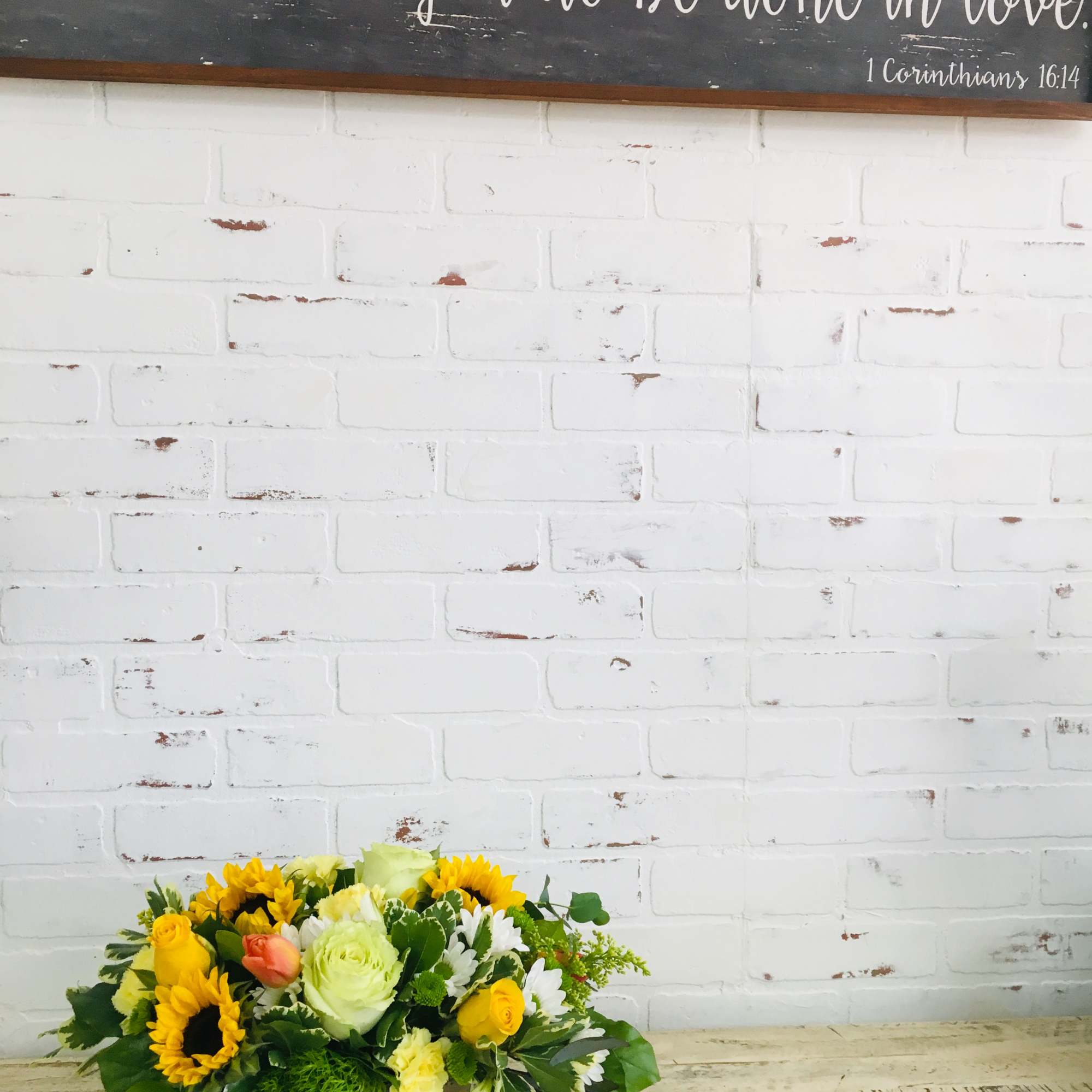 Low arrangement of yellow sunflowers, roses, and white blooms in a white wooden box