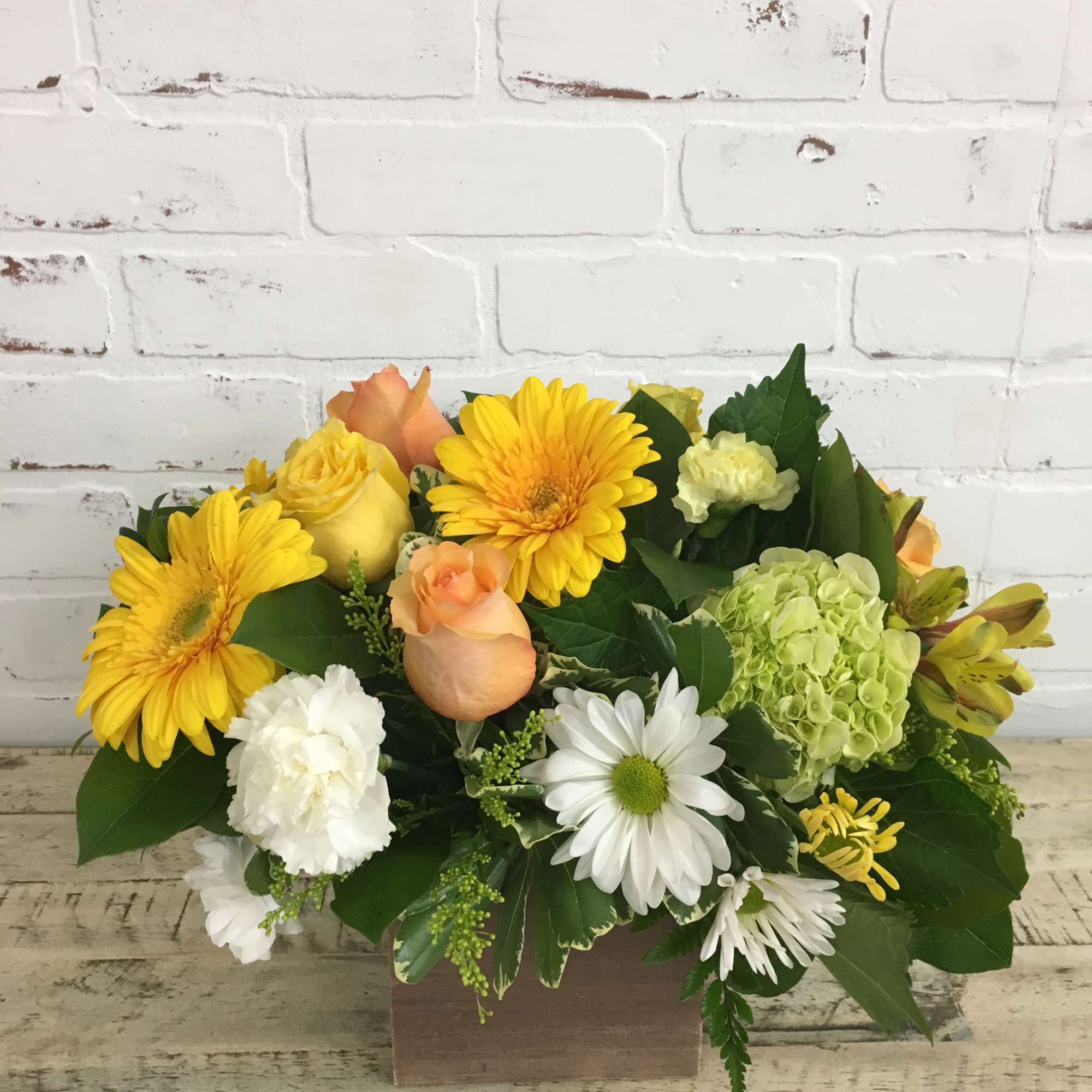 Low yellow and white flower arrangement with roses, gerbera daisies, and daisies in a wooden box