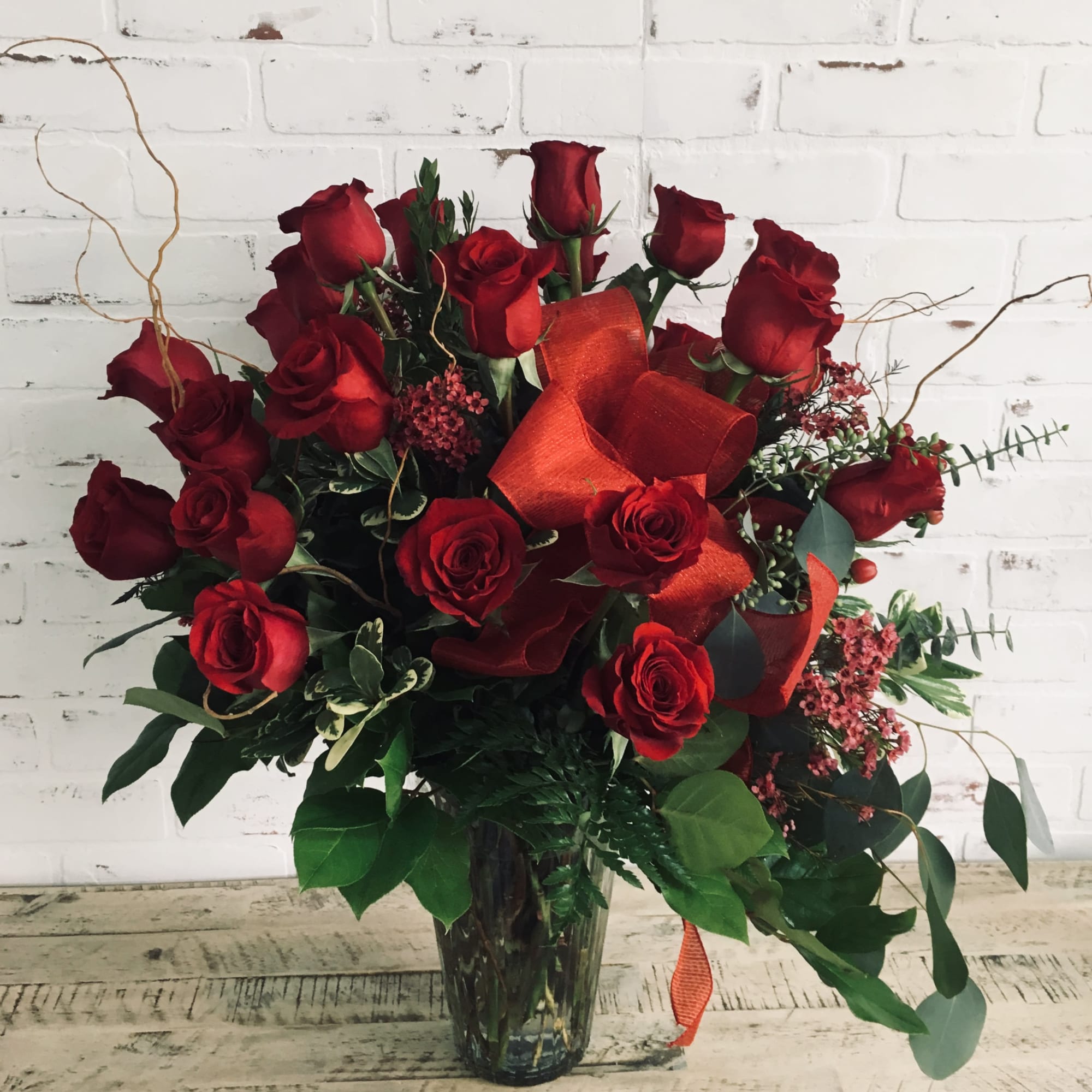 Red roses arranged in a clear glass vase with orange ribbon accents