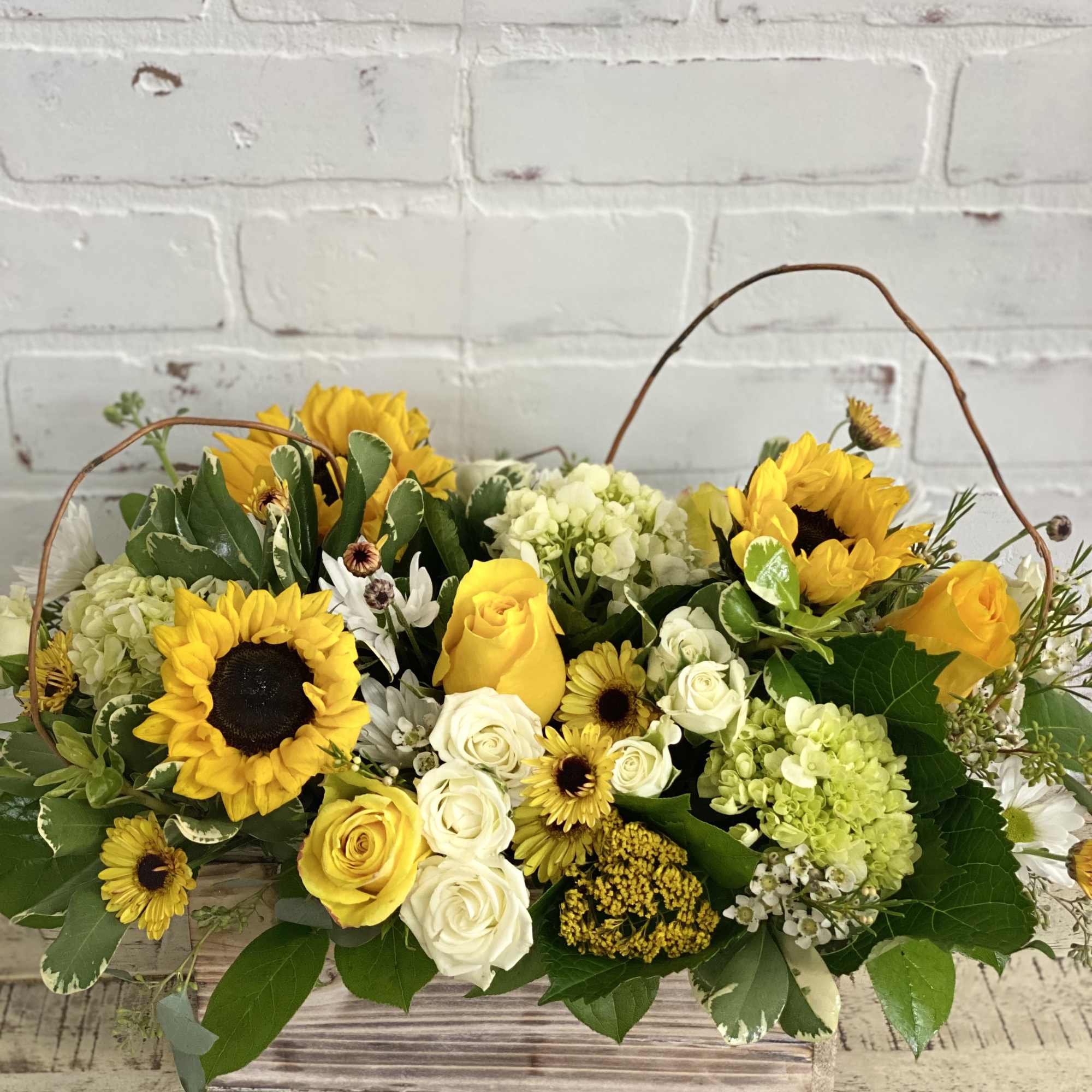 Low wooden box arrangement with yellow sunflowers, roses, white blooms, and green hydrangeas