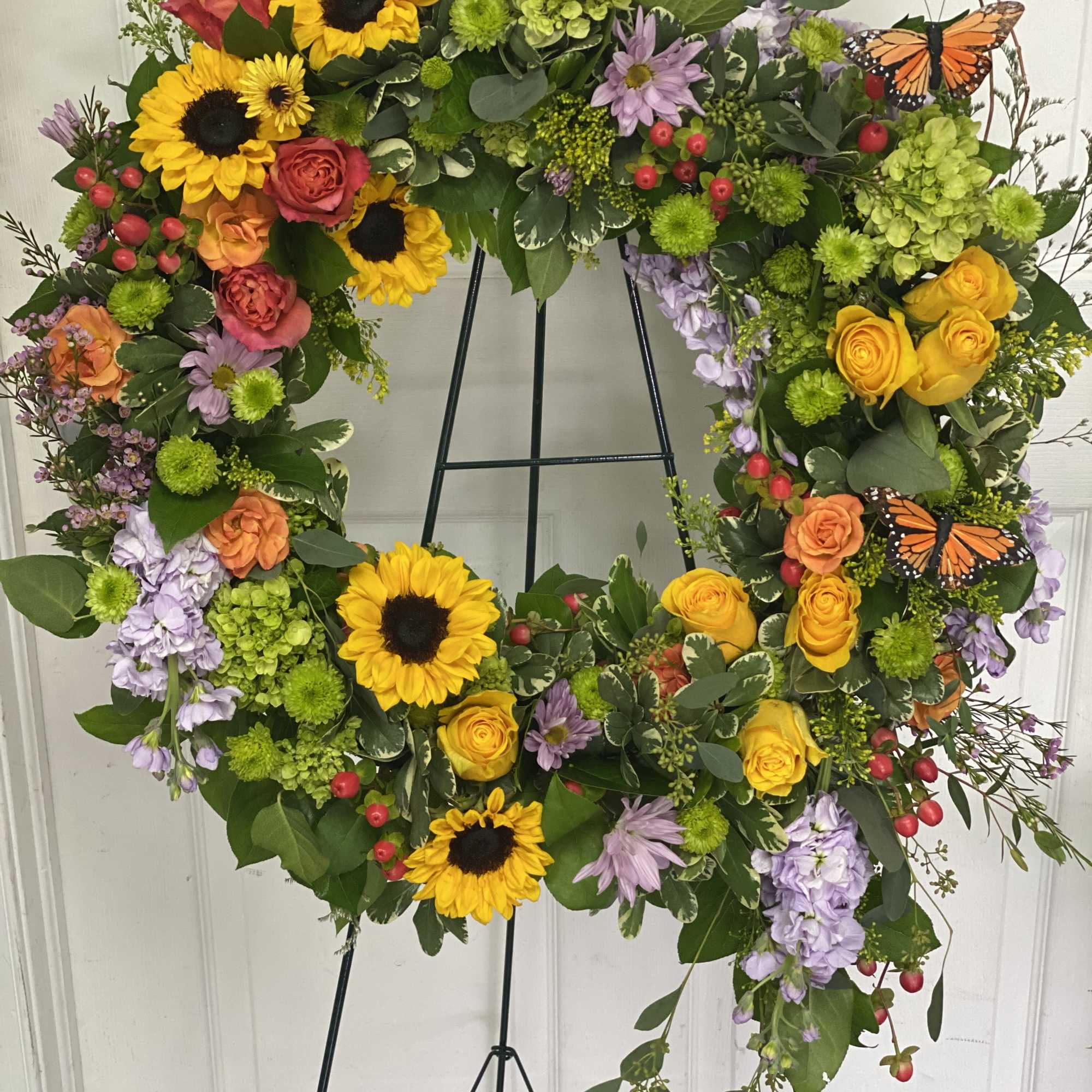 Heart-shaped floral wreath with sunflowers, roses, and butterflies on a stand