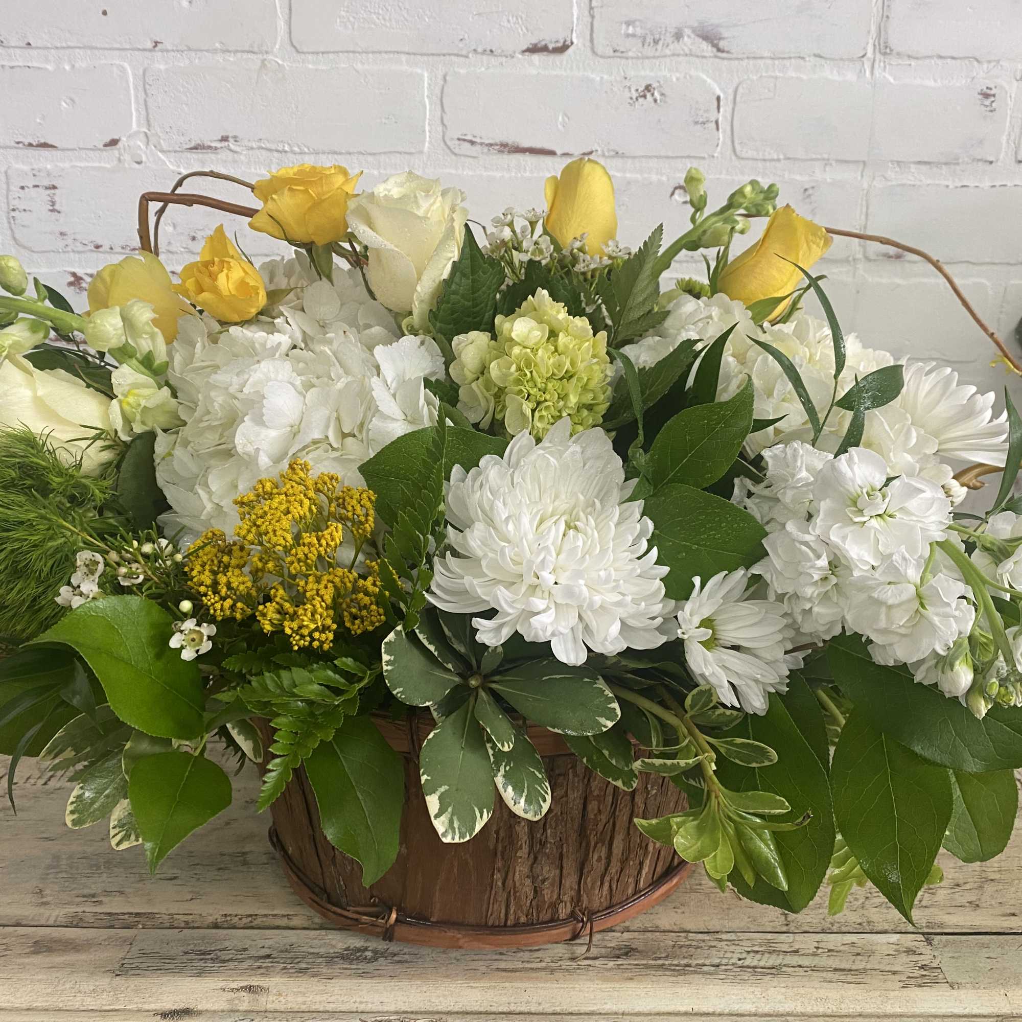 Yellow and white floral arrangement in a rustic wooden basket