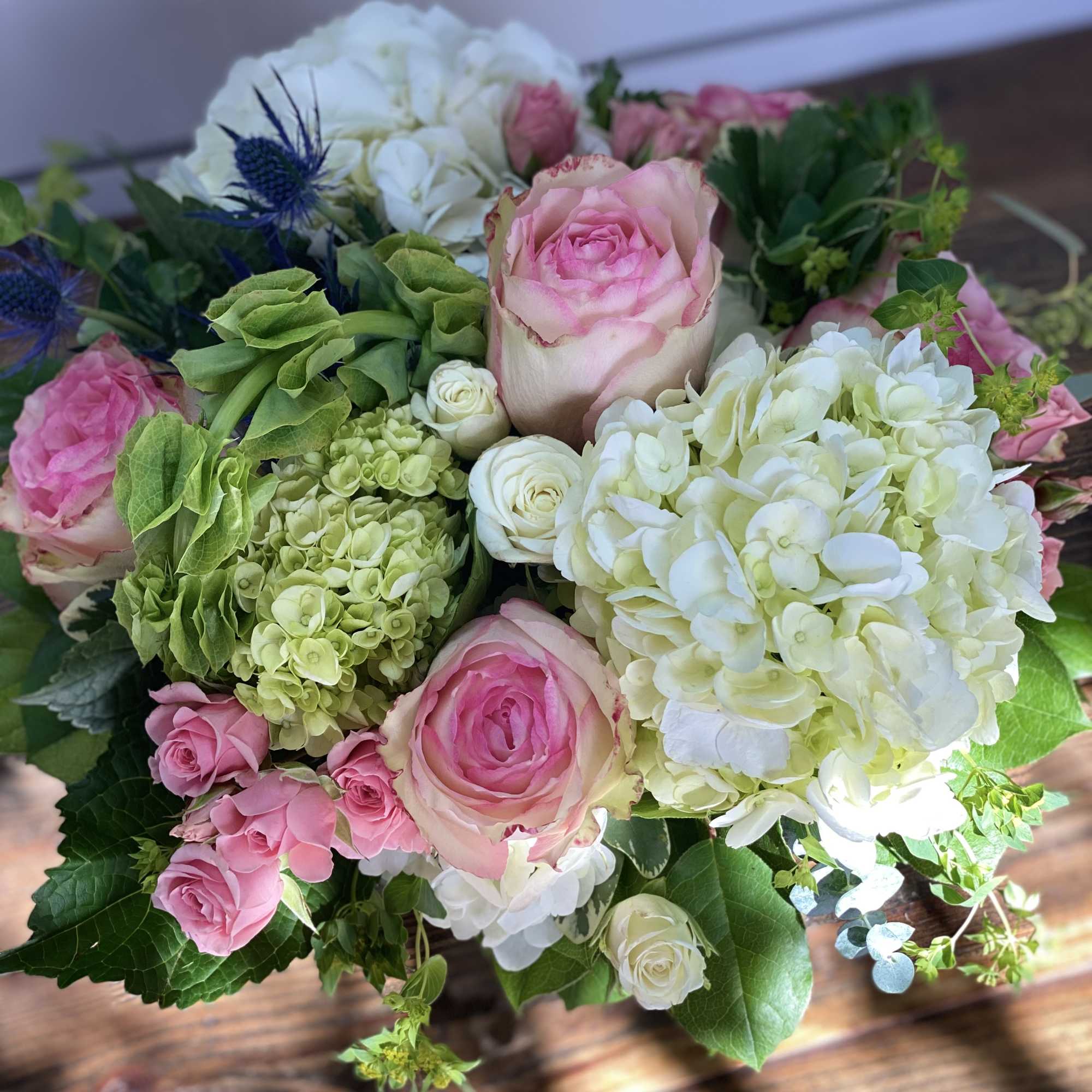 Compact bouquet of pink roses and white and green hydrangeas with blue thistle accents