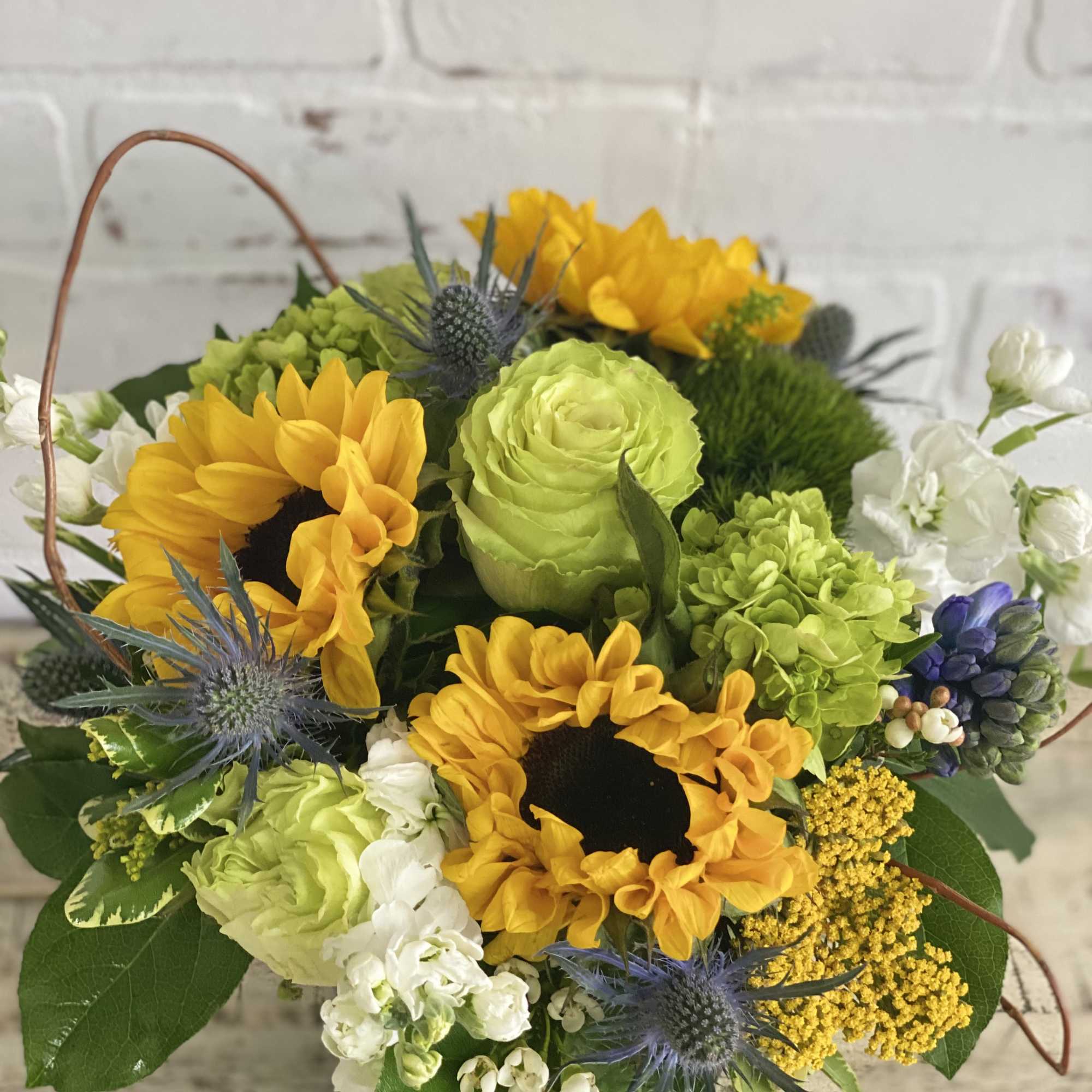 Basket arrangement with yellow sunflowers, green roses, and blue thistles