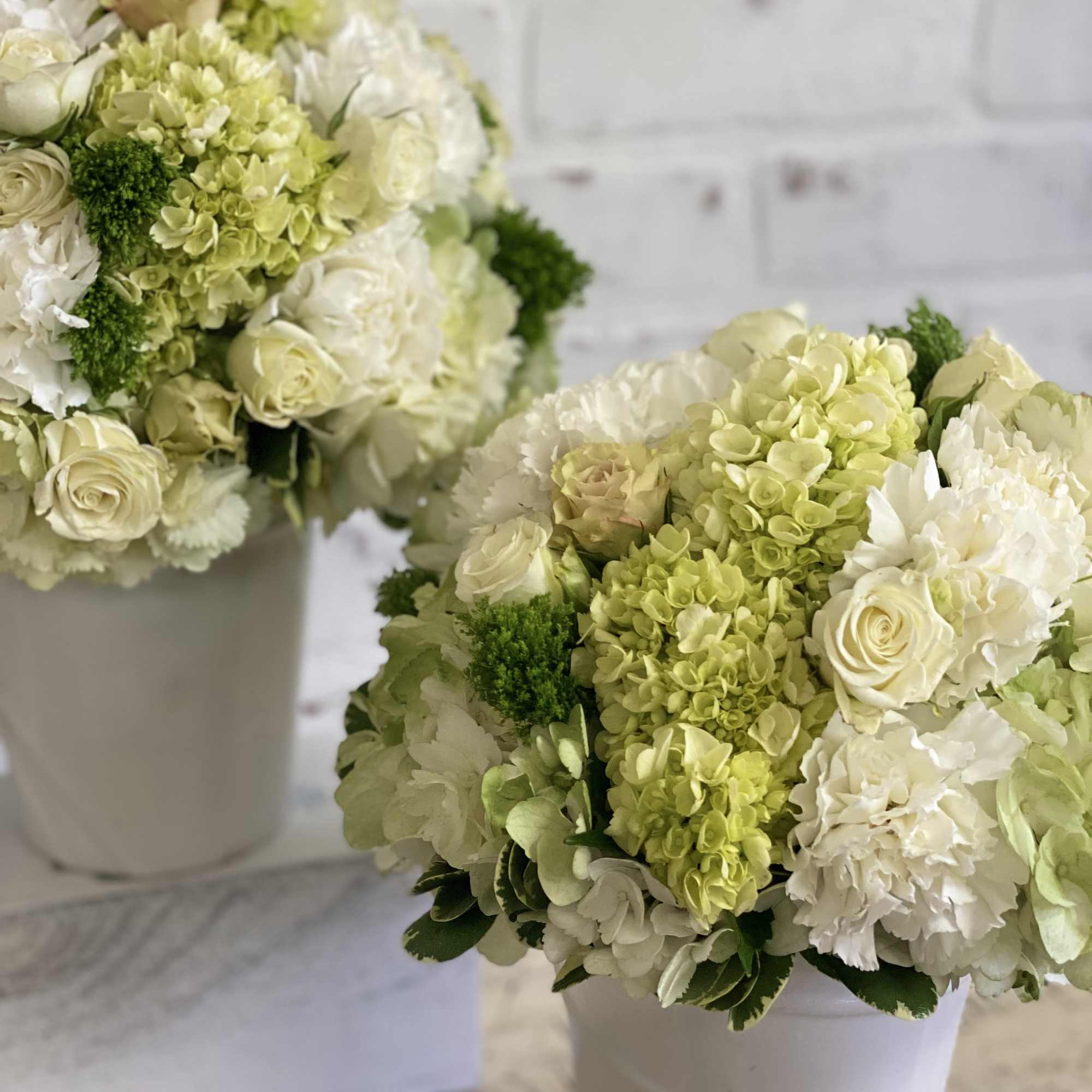 White and pale green hydrangeas, roses, and carnations arranged in white bucket-style vases.