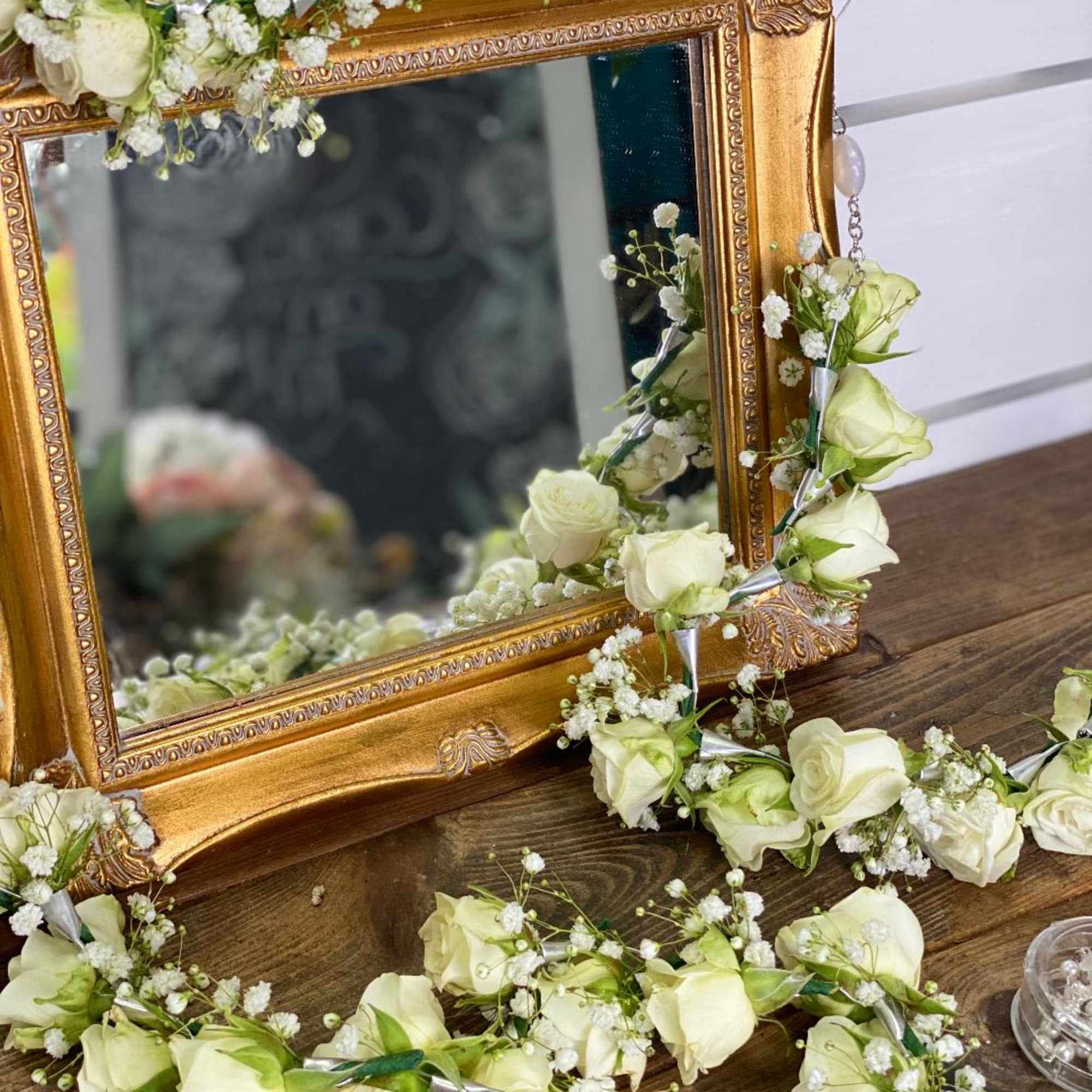 White rose garlands draped around an ornate gold mirror