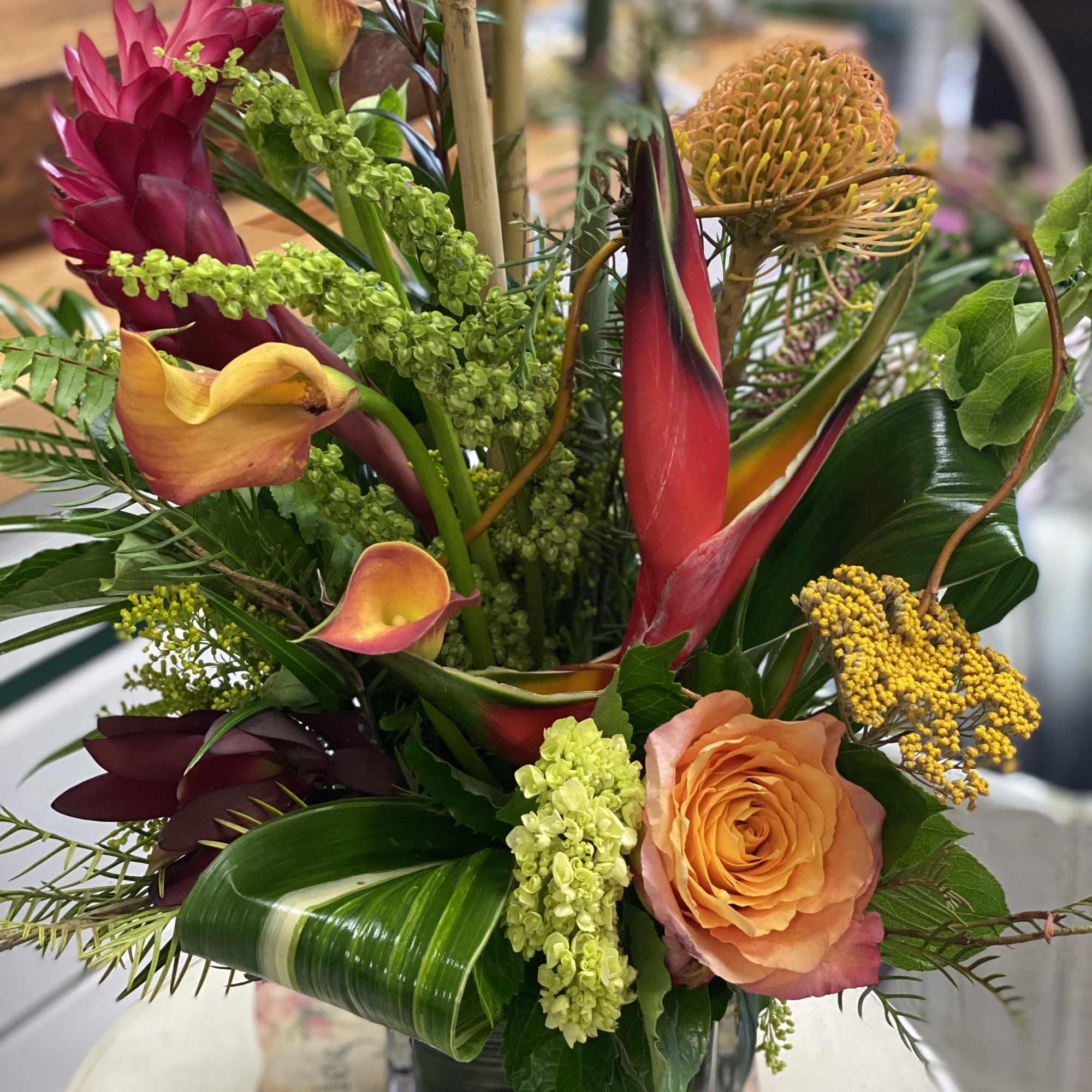 Tropical bouquet with orange roses, pink calla lilies, and green accents in a glass vase