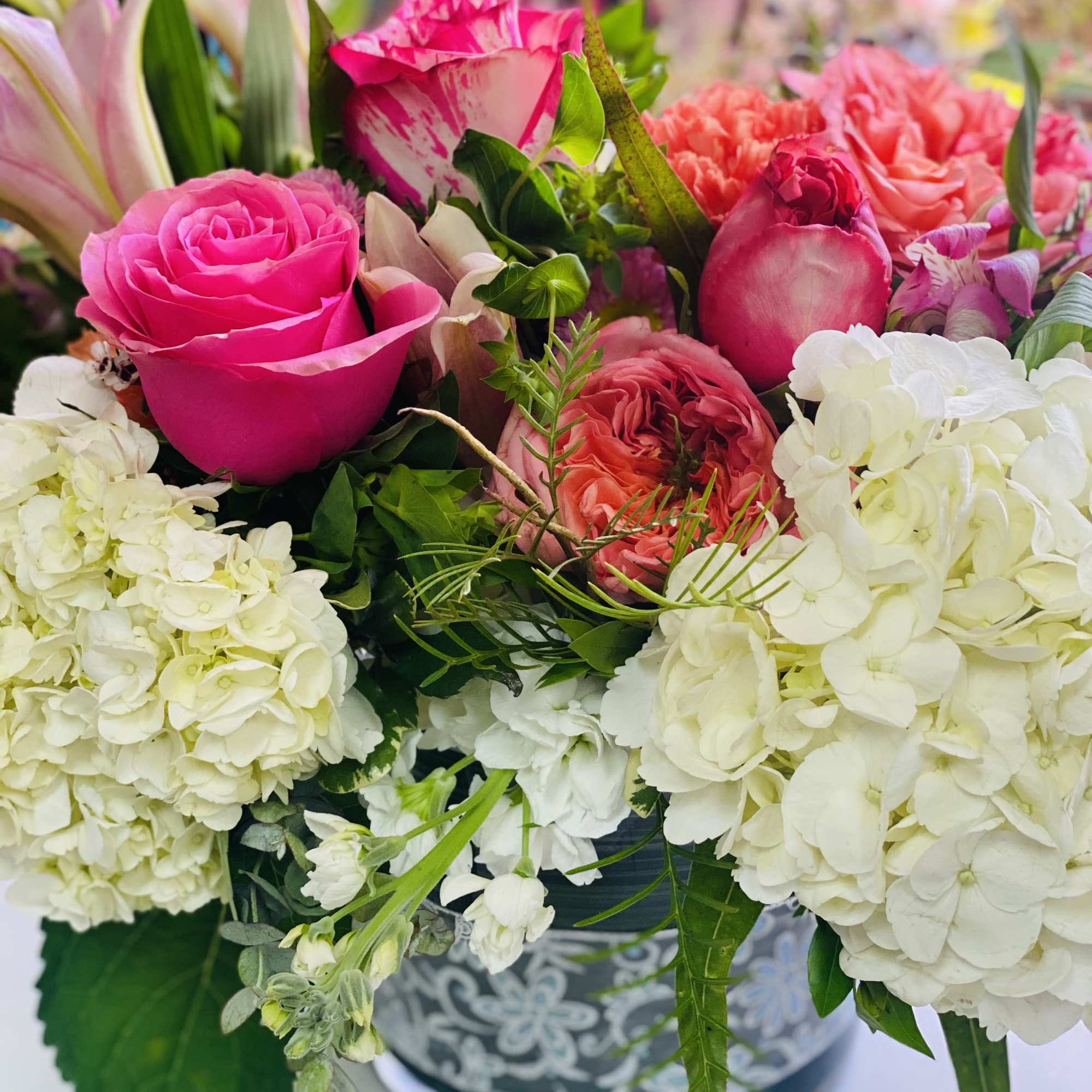 Low arrangement of bright pink roses, white hydrangeas, and coral blooms in a patterned container