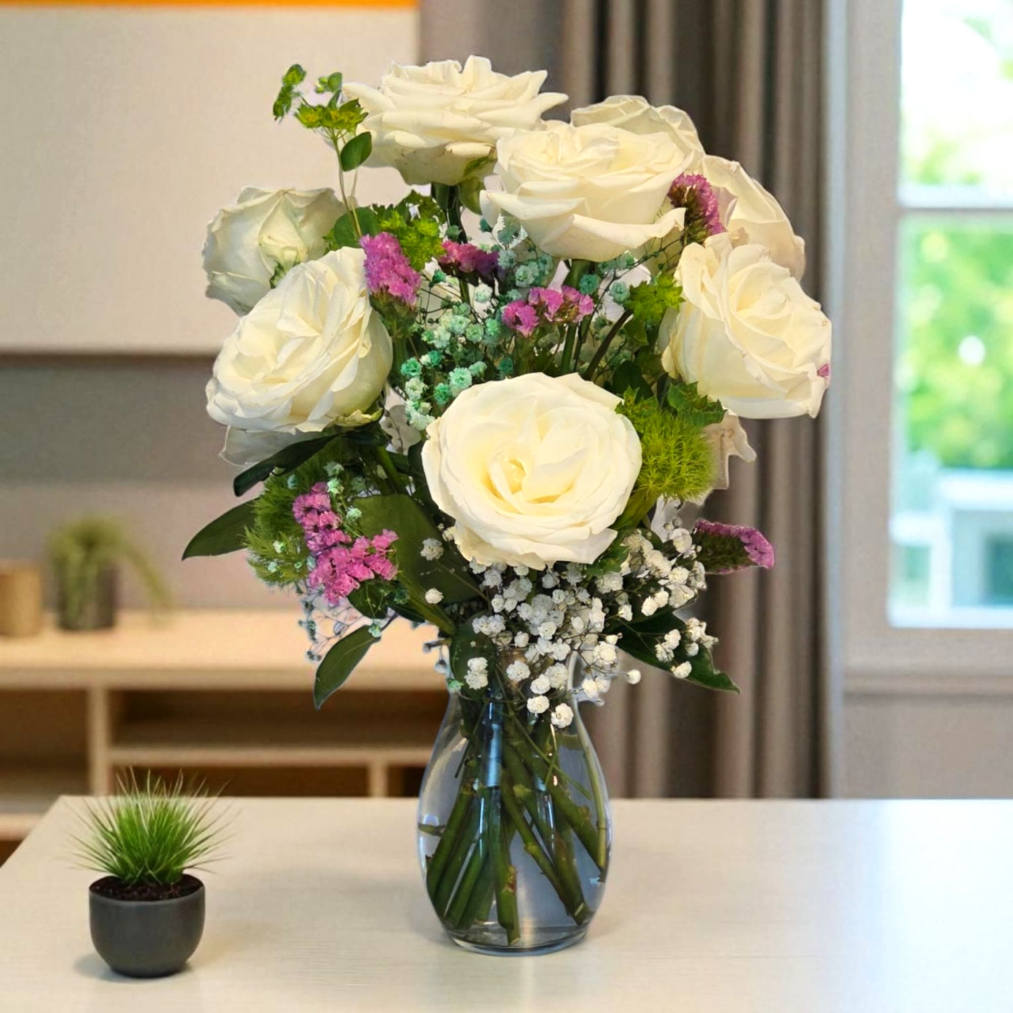 White roses in a glass vase with small purple and white filler flowers