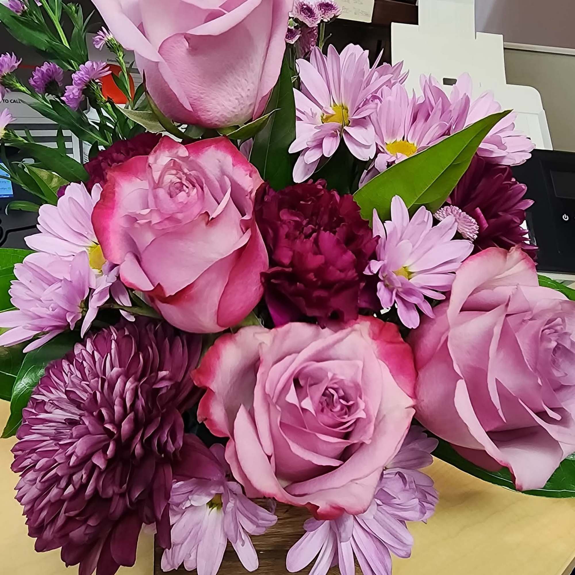 Pink roses and purple daisies arranged in a wooden box
