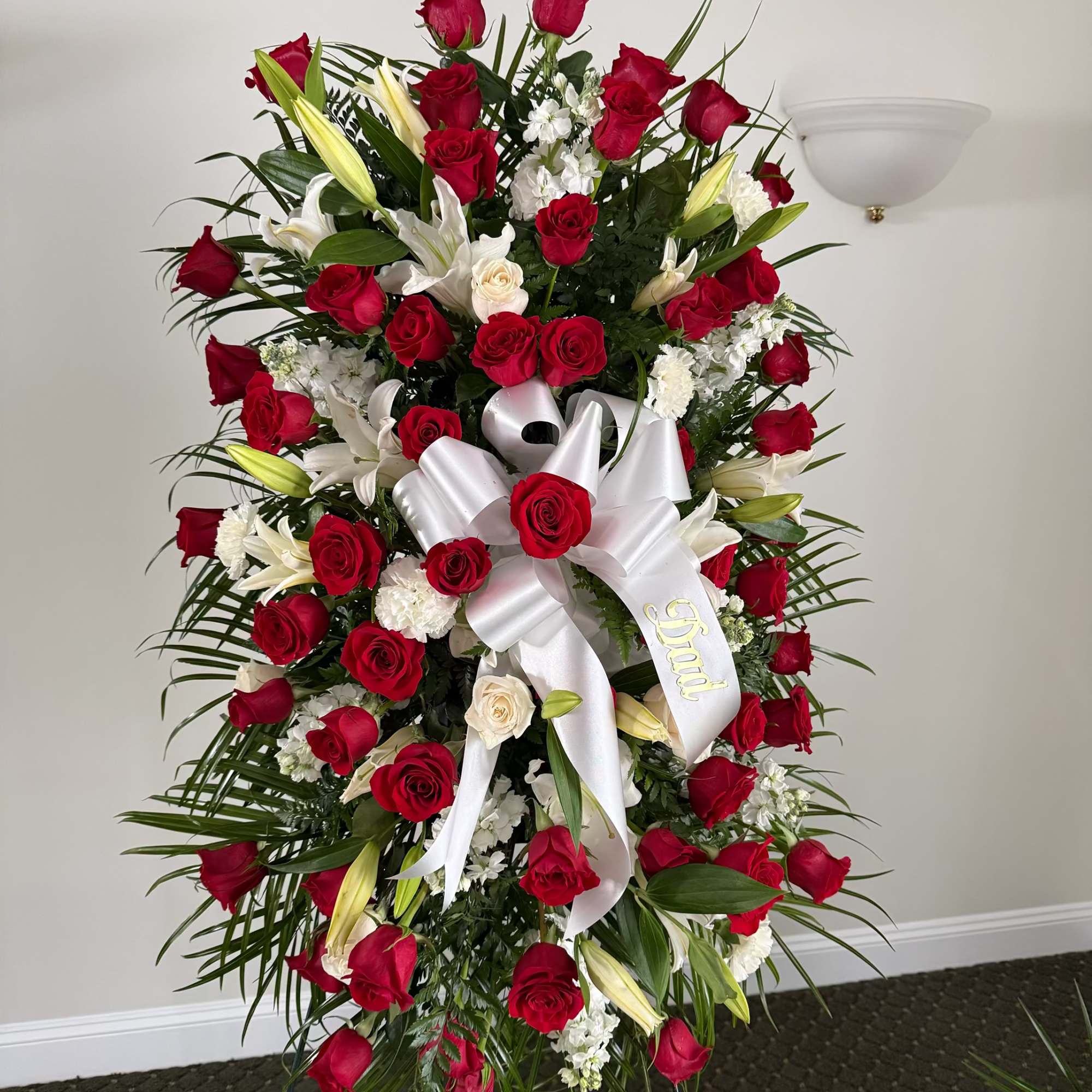 Standing floral spray of red roses and white lilies with a white ribbon bow