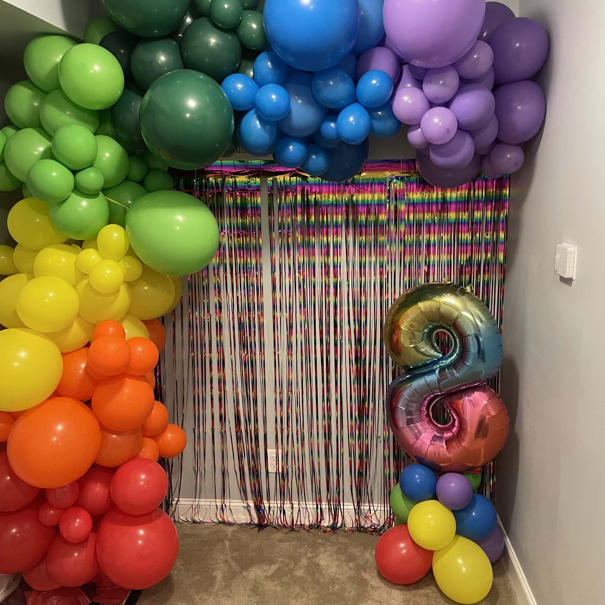 Rainbow balloon arch with a metallic number 8 balloon and fringe backdrop