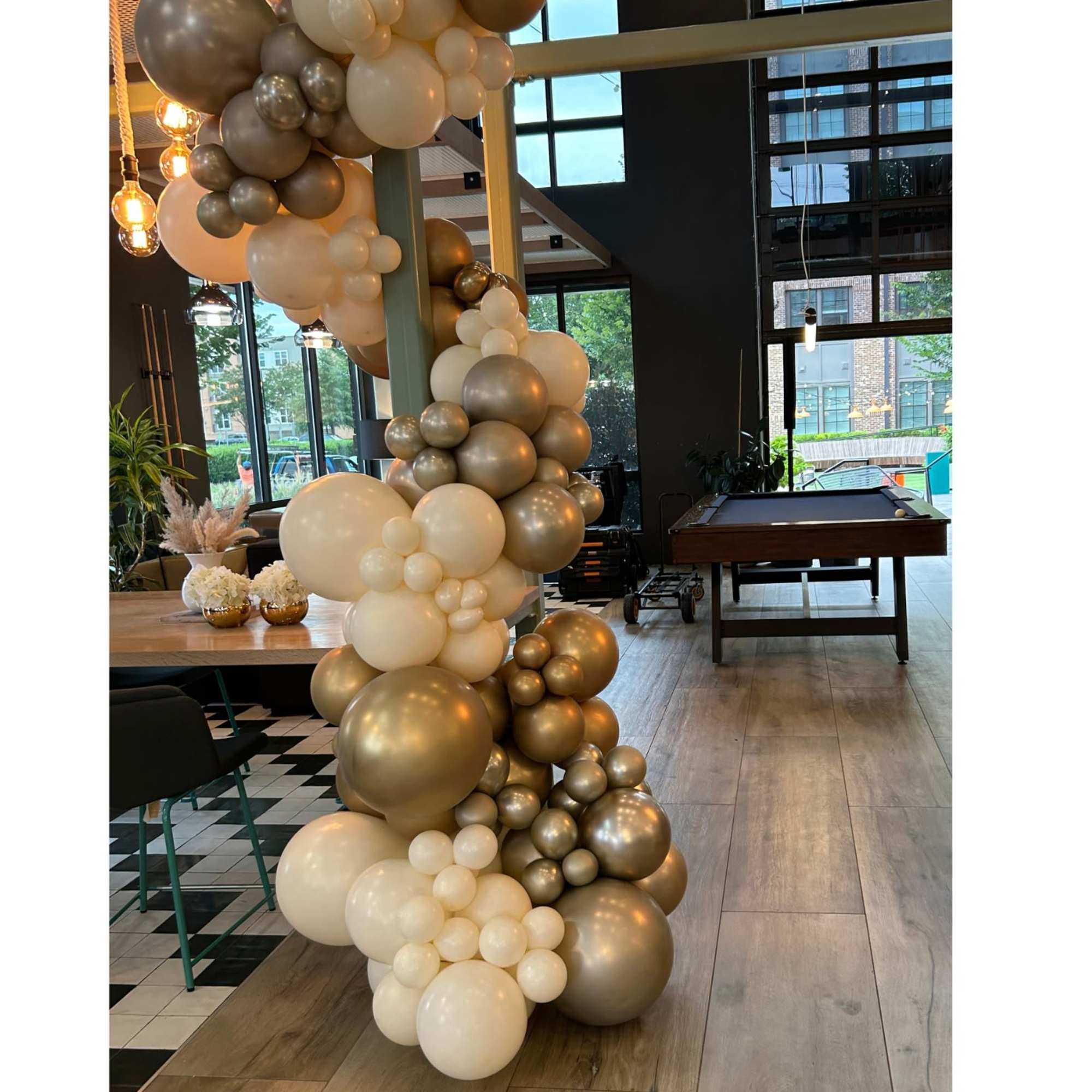 Gold and white balloon garland wrapped around a pillar indoors.