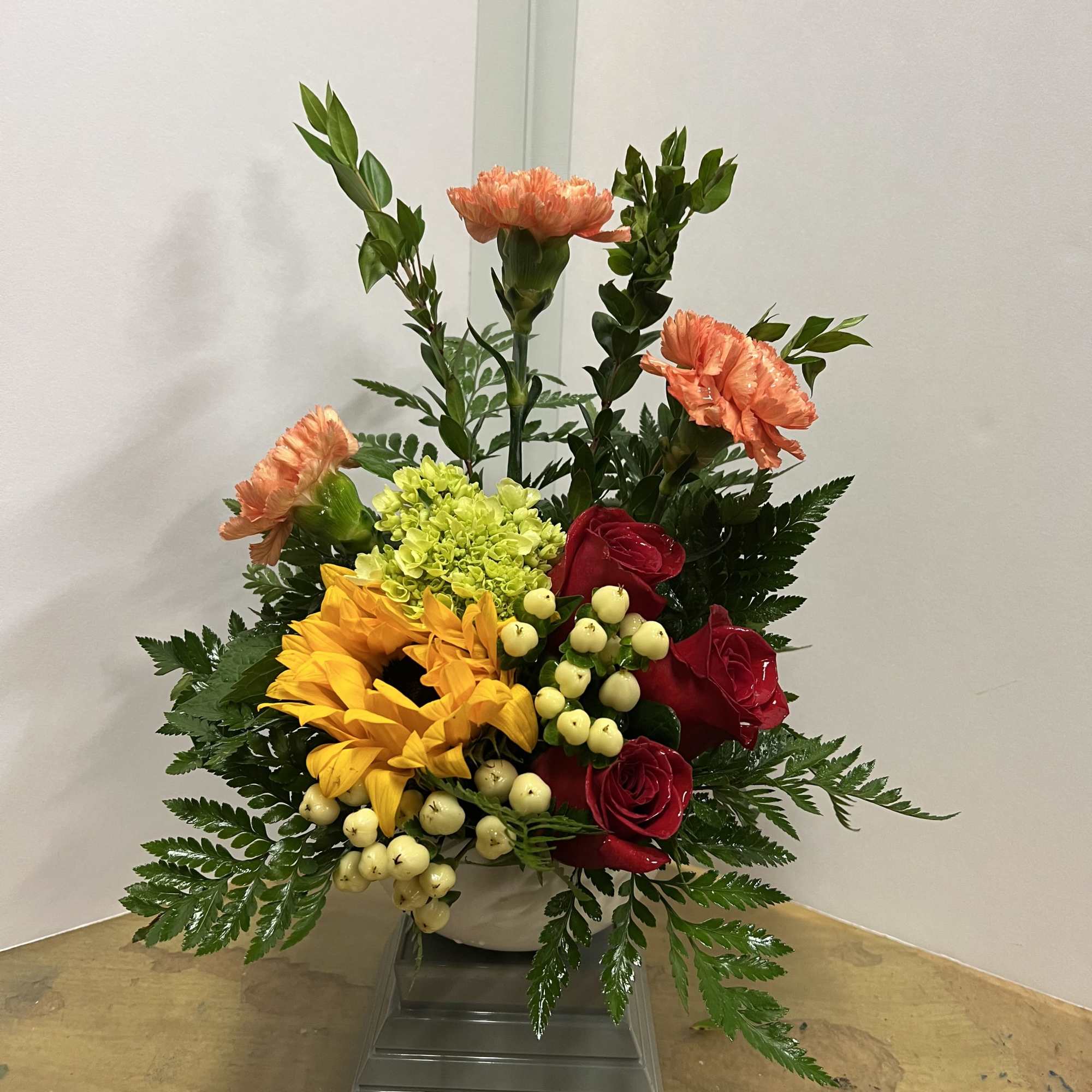 Mixed bouquet with red roses, yellow sunflowers, and peach carnations in a white vase