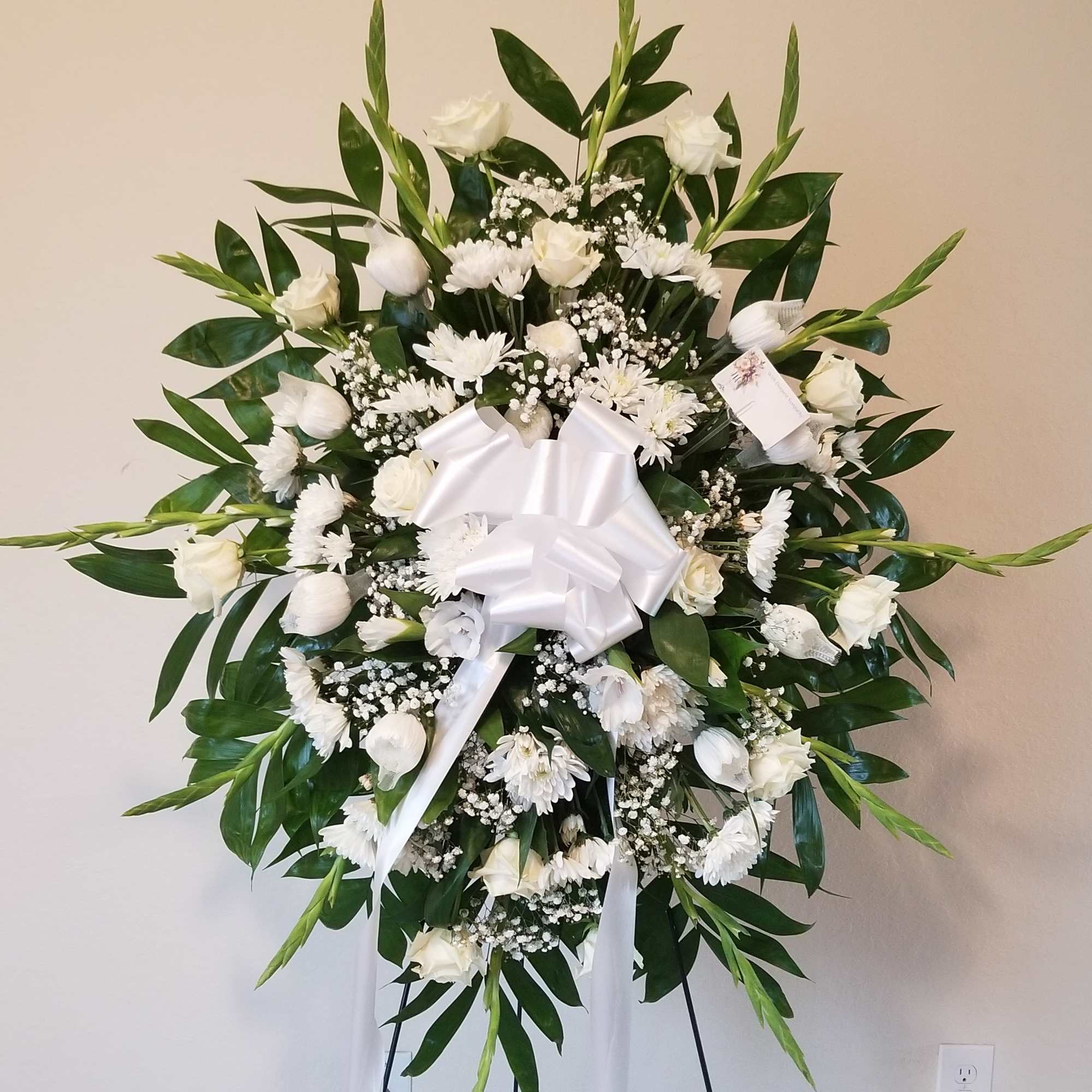 Large white funeral wreath on an easel with a satin bow