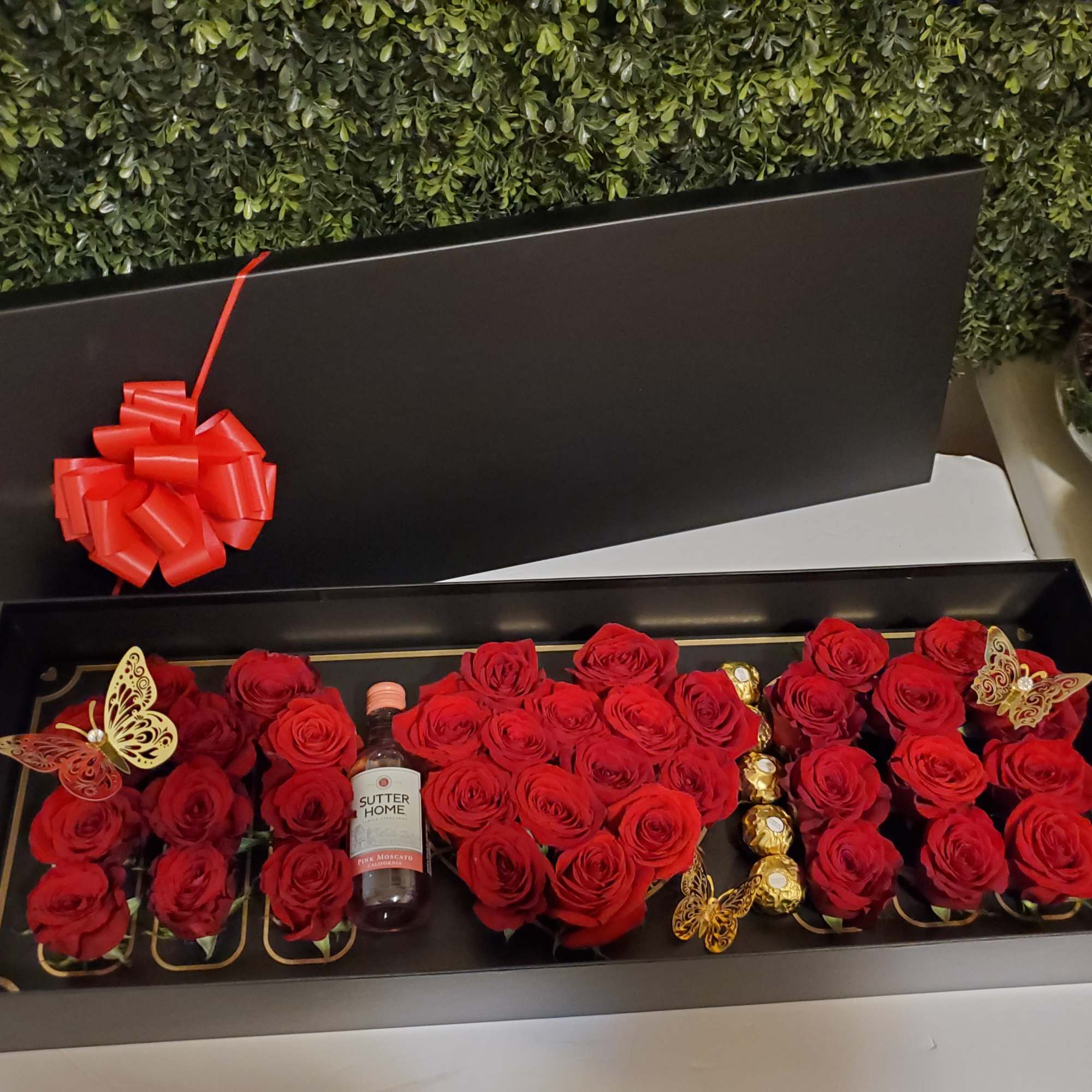 Black gift box filled with red roses, a wine bottle, and chocolates
