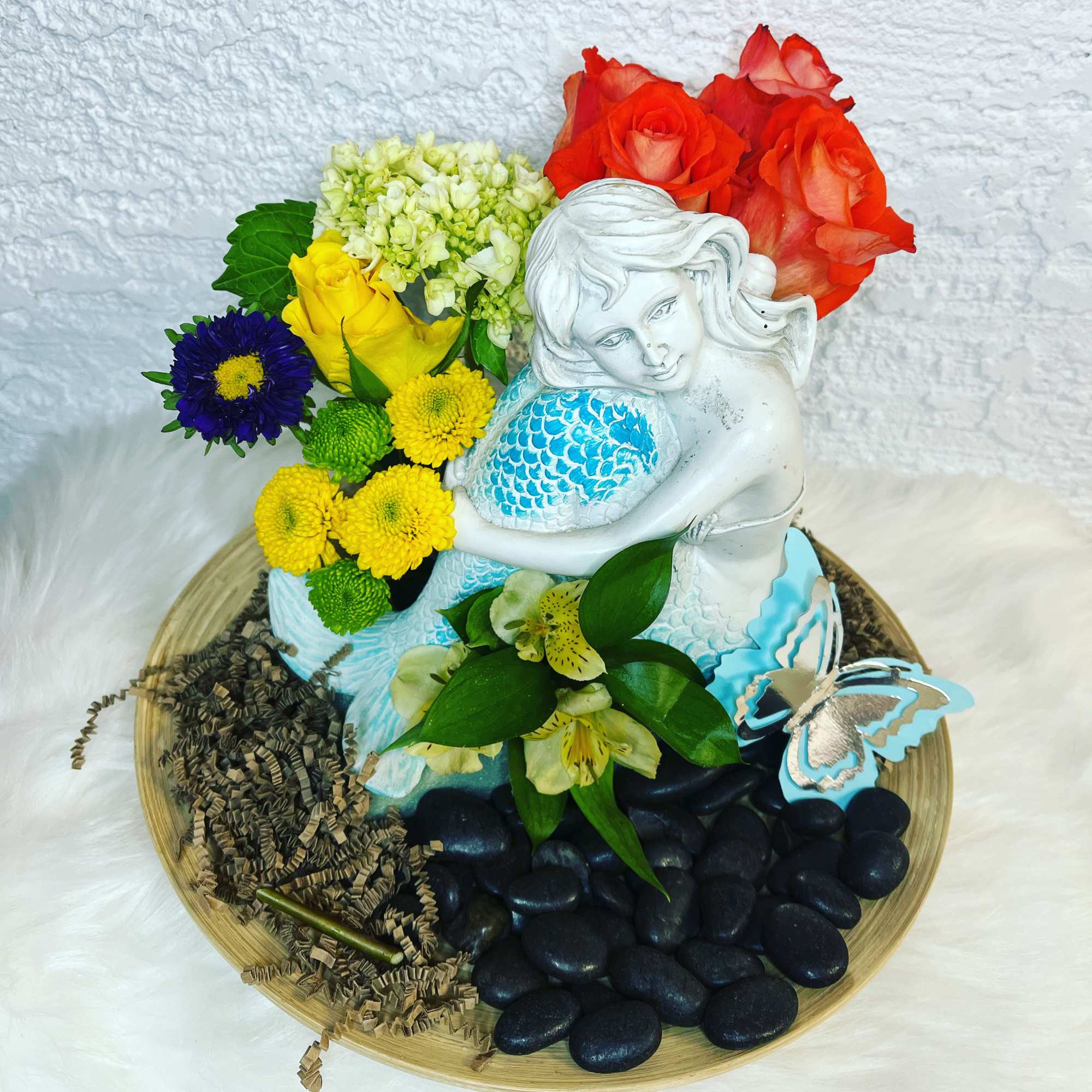 Floral arrangement with a white mermaid figurine, roses, and mixed blooms on a tray