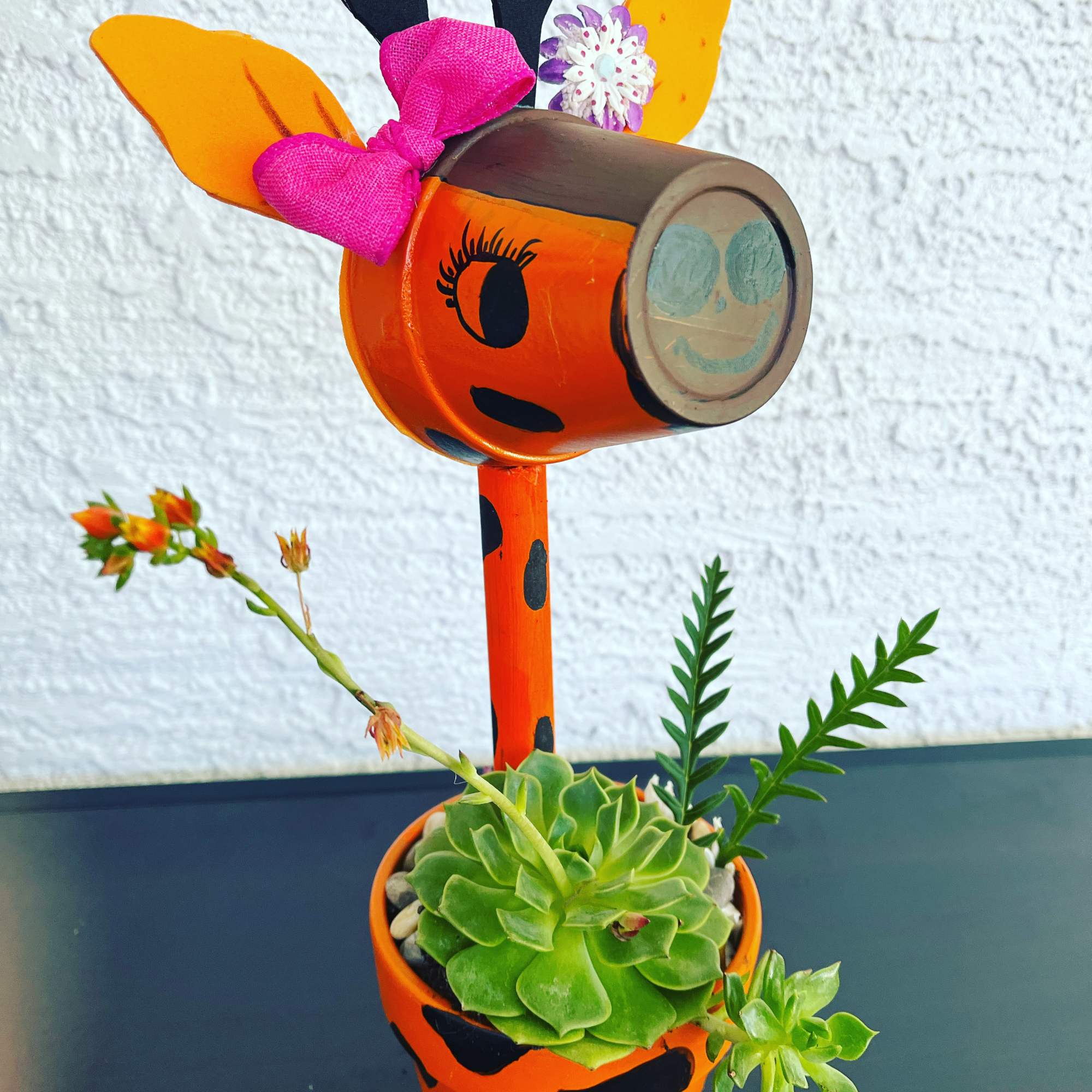 Decorative orange painted planter with a succulent and flower accents