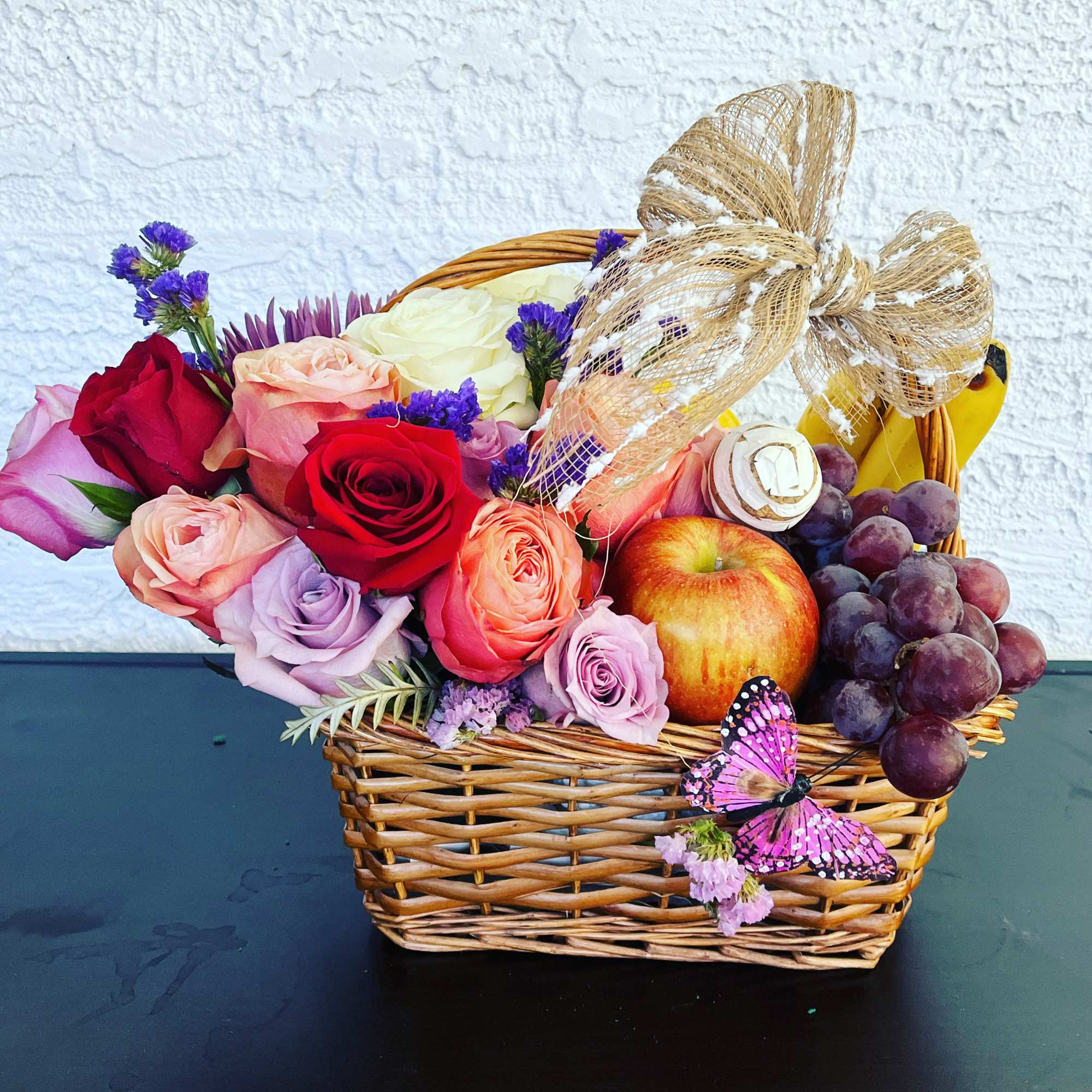 Basket of roses with fruit, grapes, and a butterfly decoration