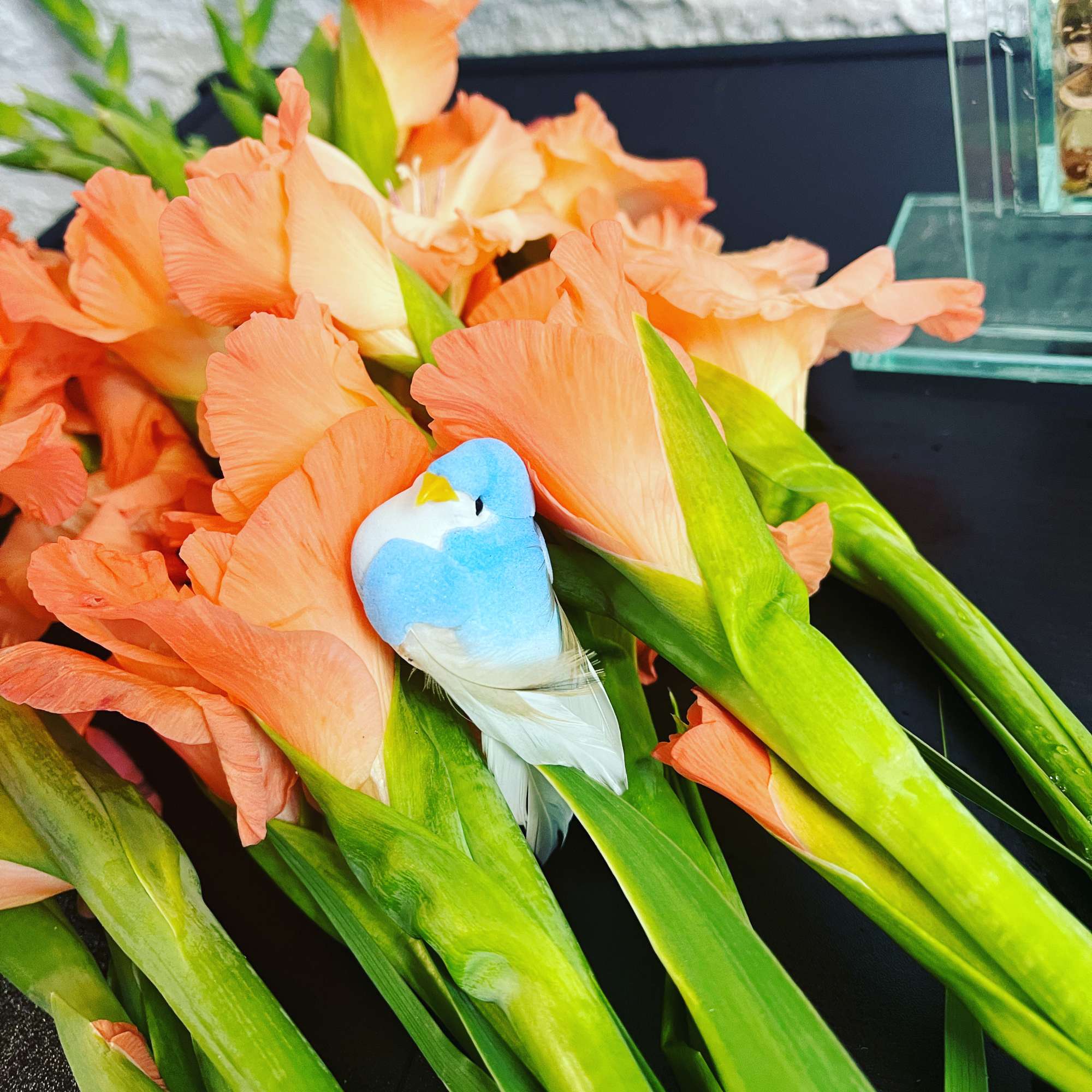 Orange gladiolus bouquet with a small blue-and-white bird ornament