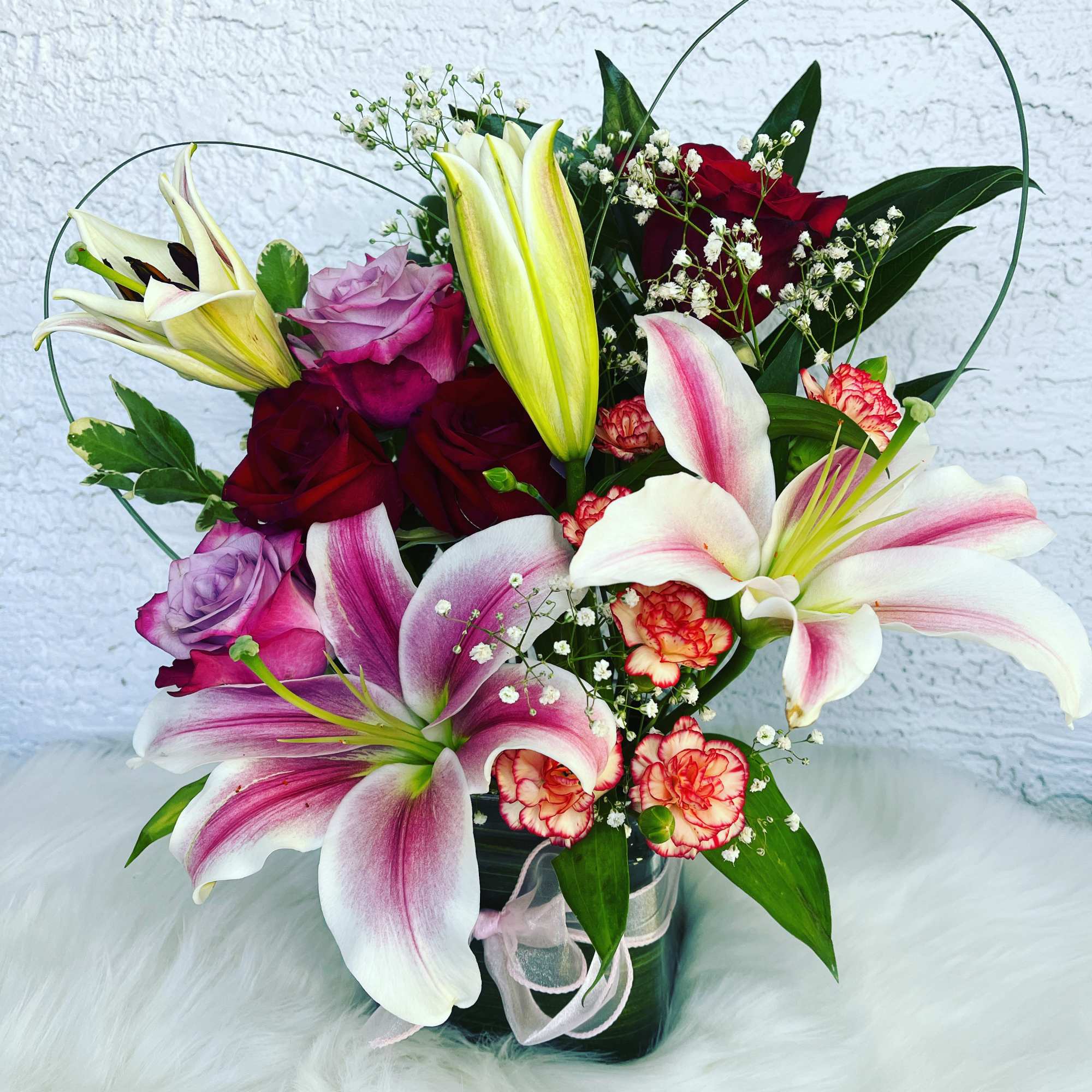 Bouquet of lilies and roses in a glass vase with pink ribbon