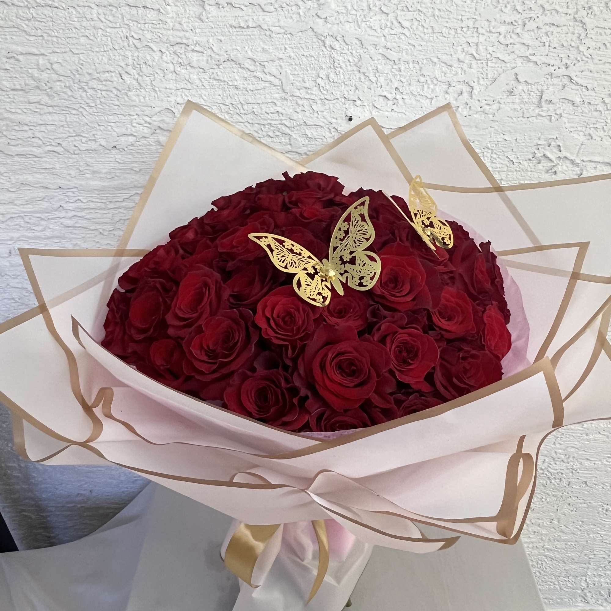 Bouquet of deep red roses wrapped in pale paper with gold butterfly accents
