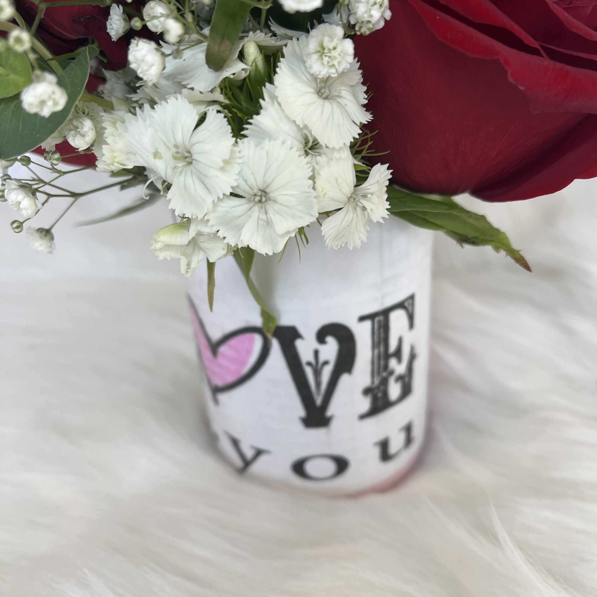 Red roses and white carnations in a white vase with "LOVE" text