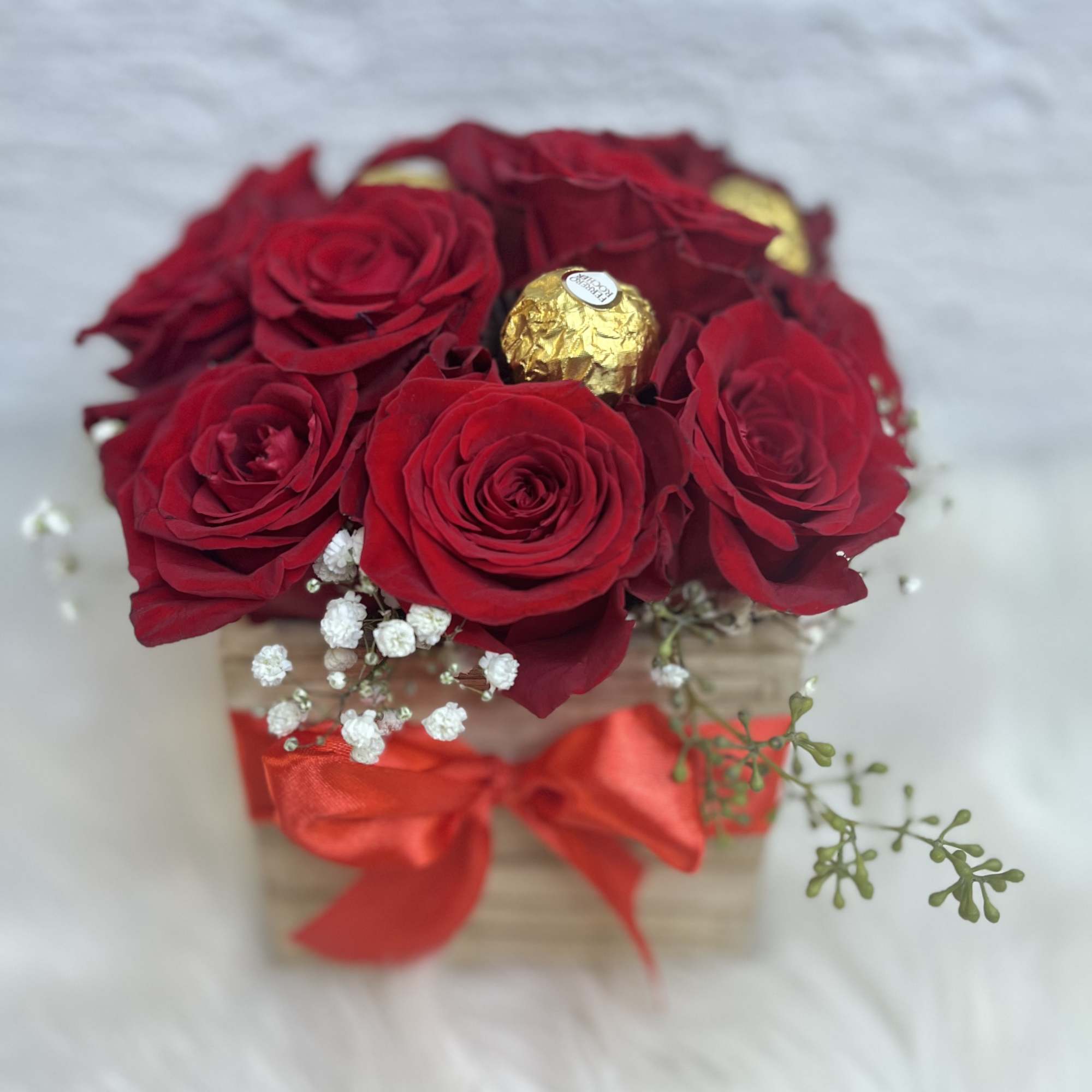 Red roses in a small box with a red ribbon and gold chocolates