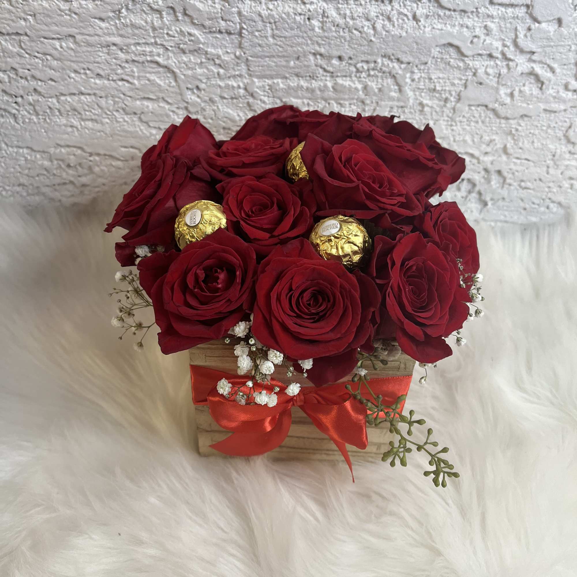 Red roses in a wooden box with gold-wrapped chocolates and a red ribbon